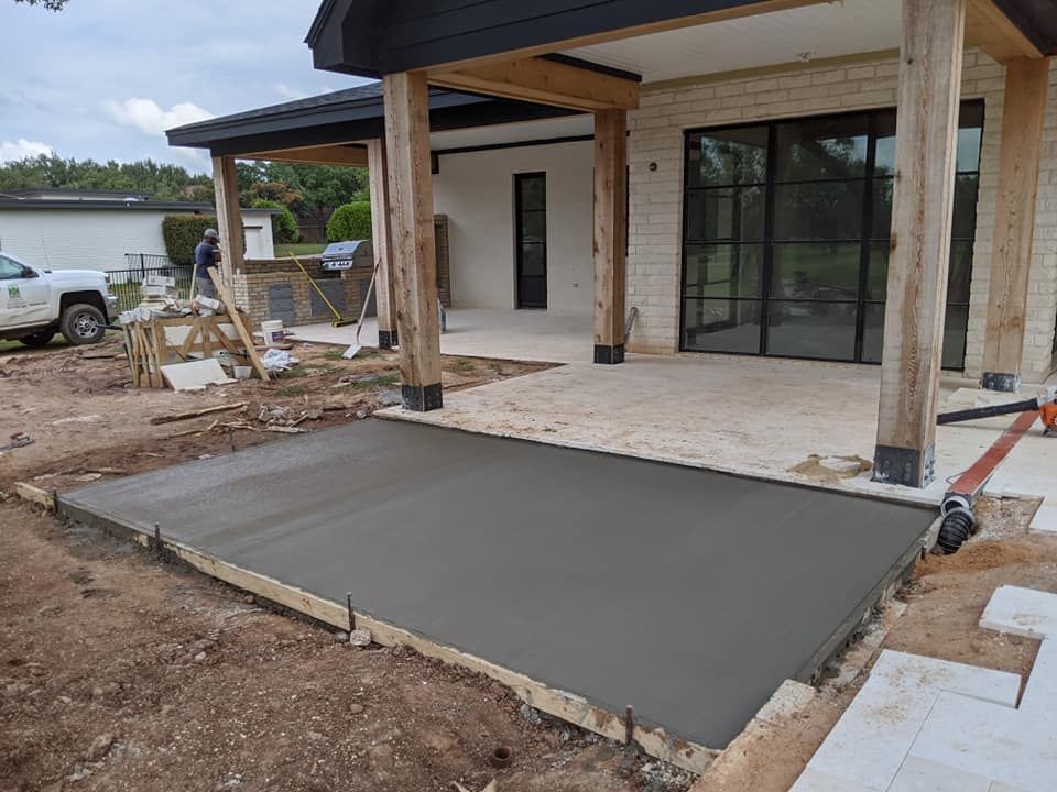 Freshly poured concrete patio beside a house with wooden beams and large glass doors.