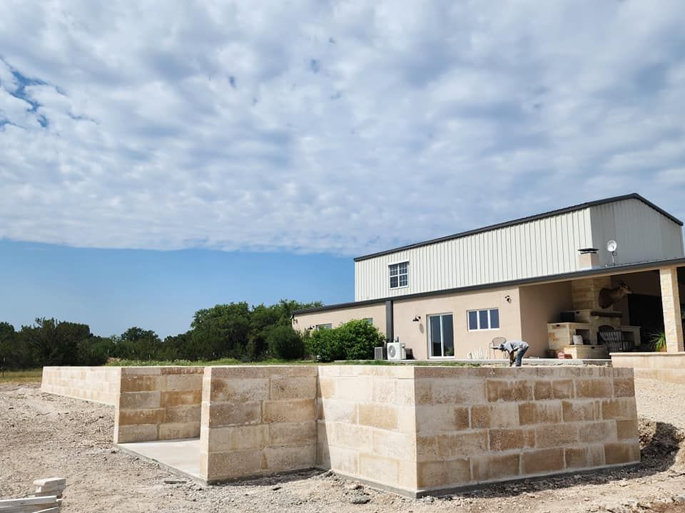 Stone foundation being built in front of a light-colored building under a partly cloudy sky.