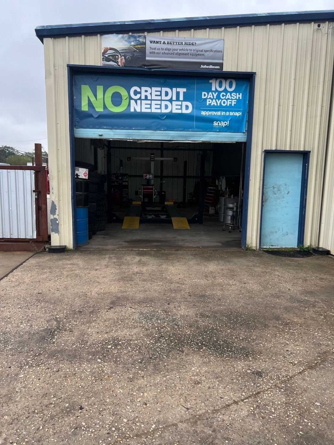Exterior view of a car repair shop with an open garage door; sign says 