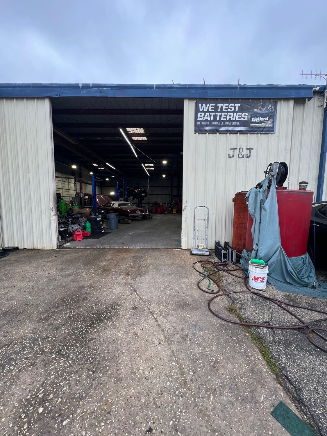 Exterior of a garage: open bay door, cars inside, sign above reads 
