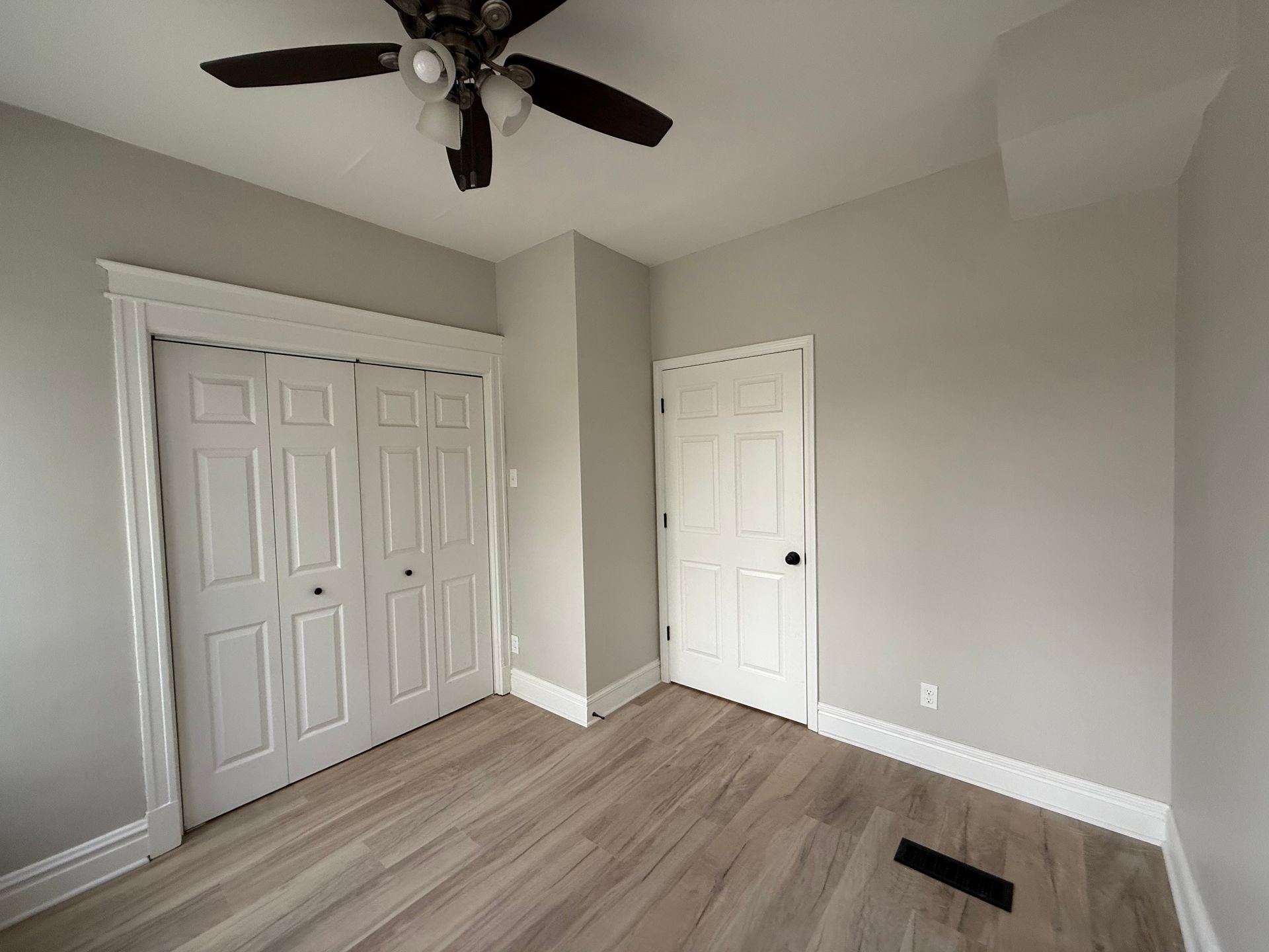 Bedroom interior with light wood-look flooring, white trim, and gray walls. Includes a closet and a door.