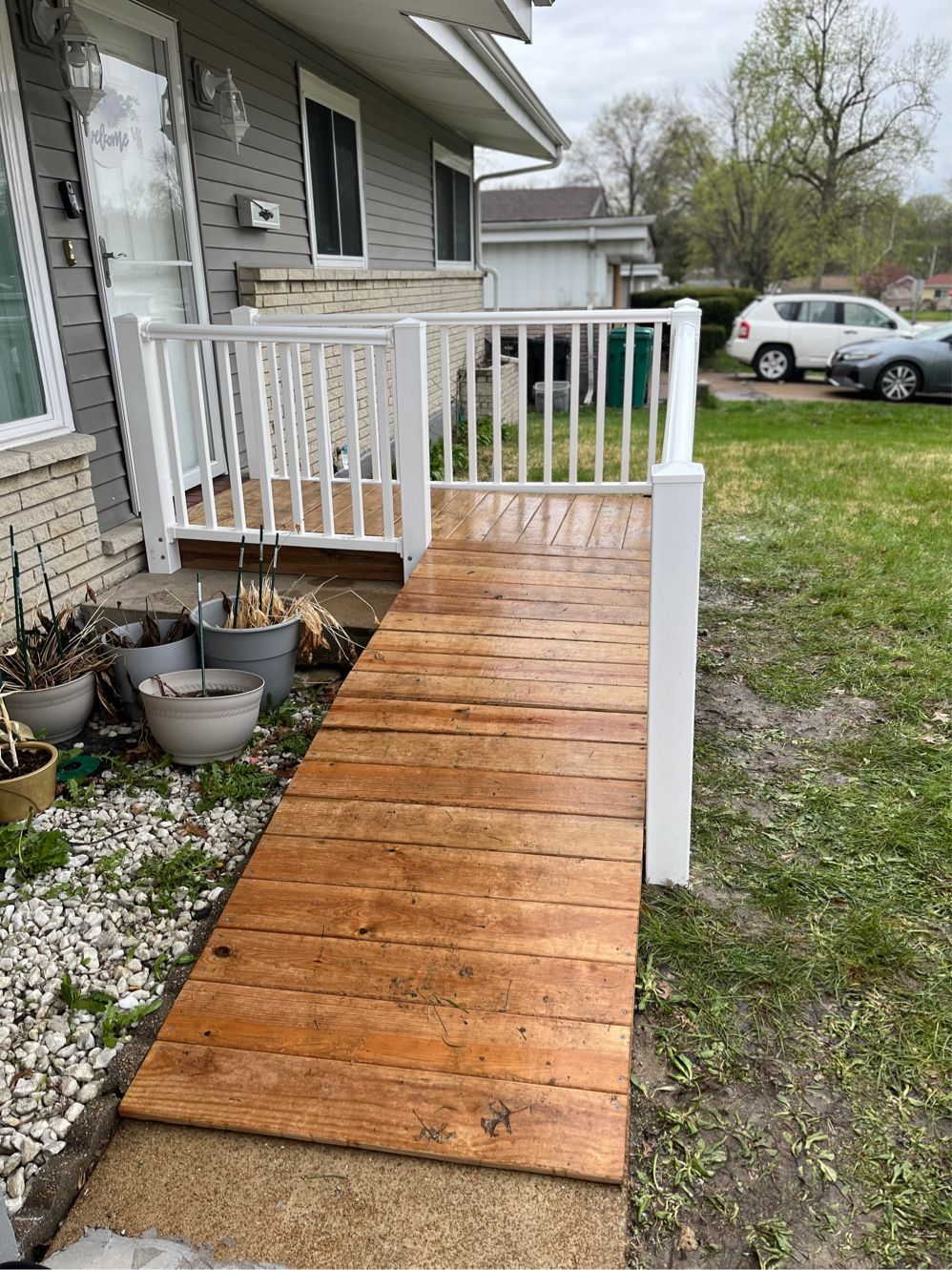 Wooden ramp with white railing leading to a house entrance. Green grass surrounds.