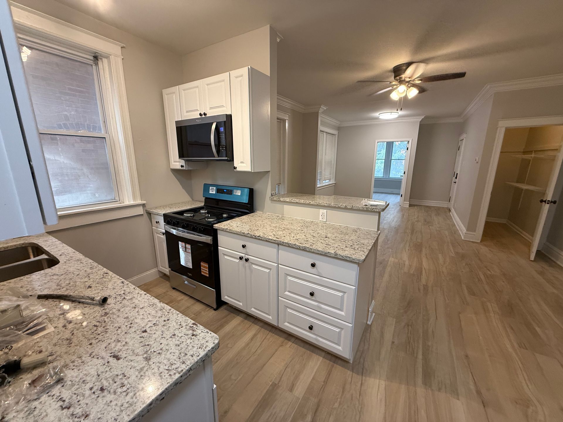 Kitchen with white cabinets, granite countertops, and light wood floors, leading into a living space.