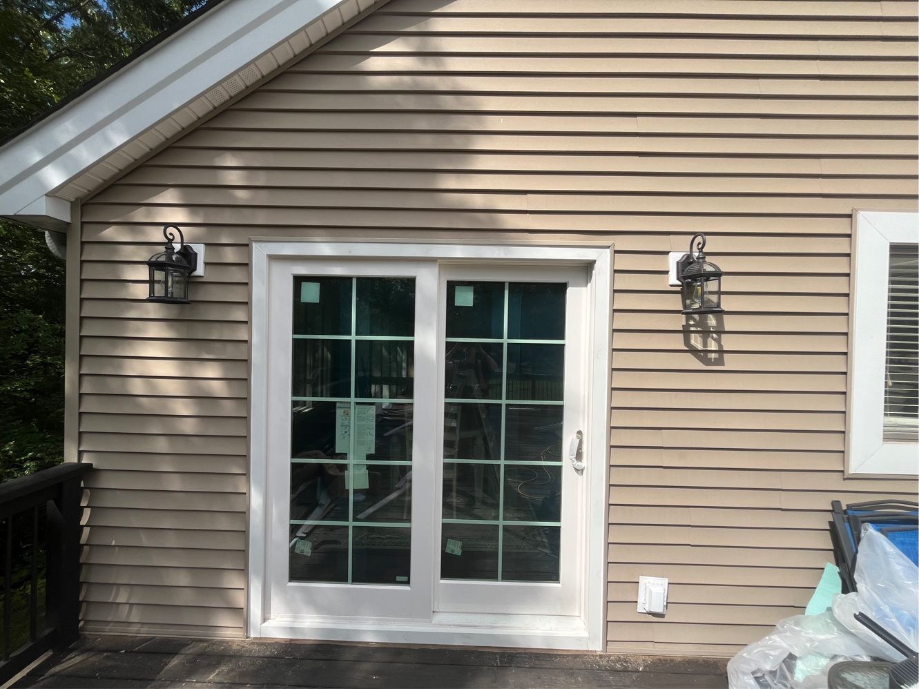Tan siding with white-framed French doors. Black sconces flank the doors. A deck is visible on the left.