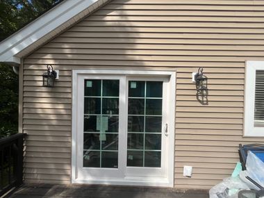 Tan siding with white-framed French doors. Black sconces flank the doors. A deck is visible on the left.