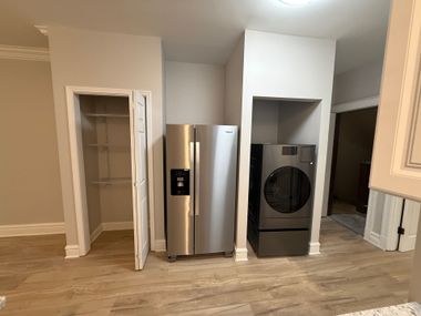 Kitchen area with pantry, refrigerator, and washer/dryer in built-in alcoves. Light wood floors and neutral walls.