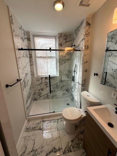 Modern bathroom with white marble tile shower, toilet, sink, and vanity. Black fixtures.