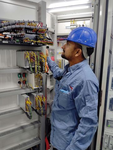 Man in blue hard hat inspecting electrical panel.