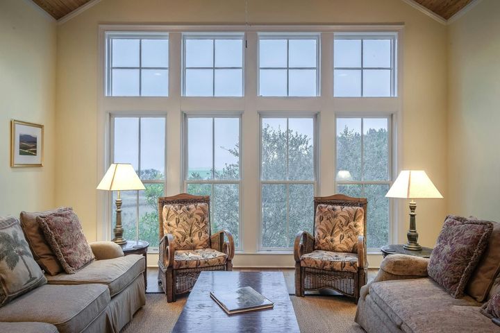 Living room with large windows, two sofas, two armchairs, two lamps, and a coffee table.