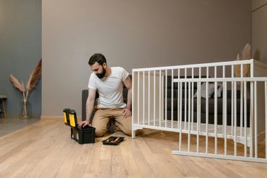 Man kneeling on floor assembling crib from toolbox.