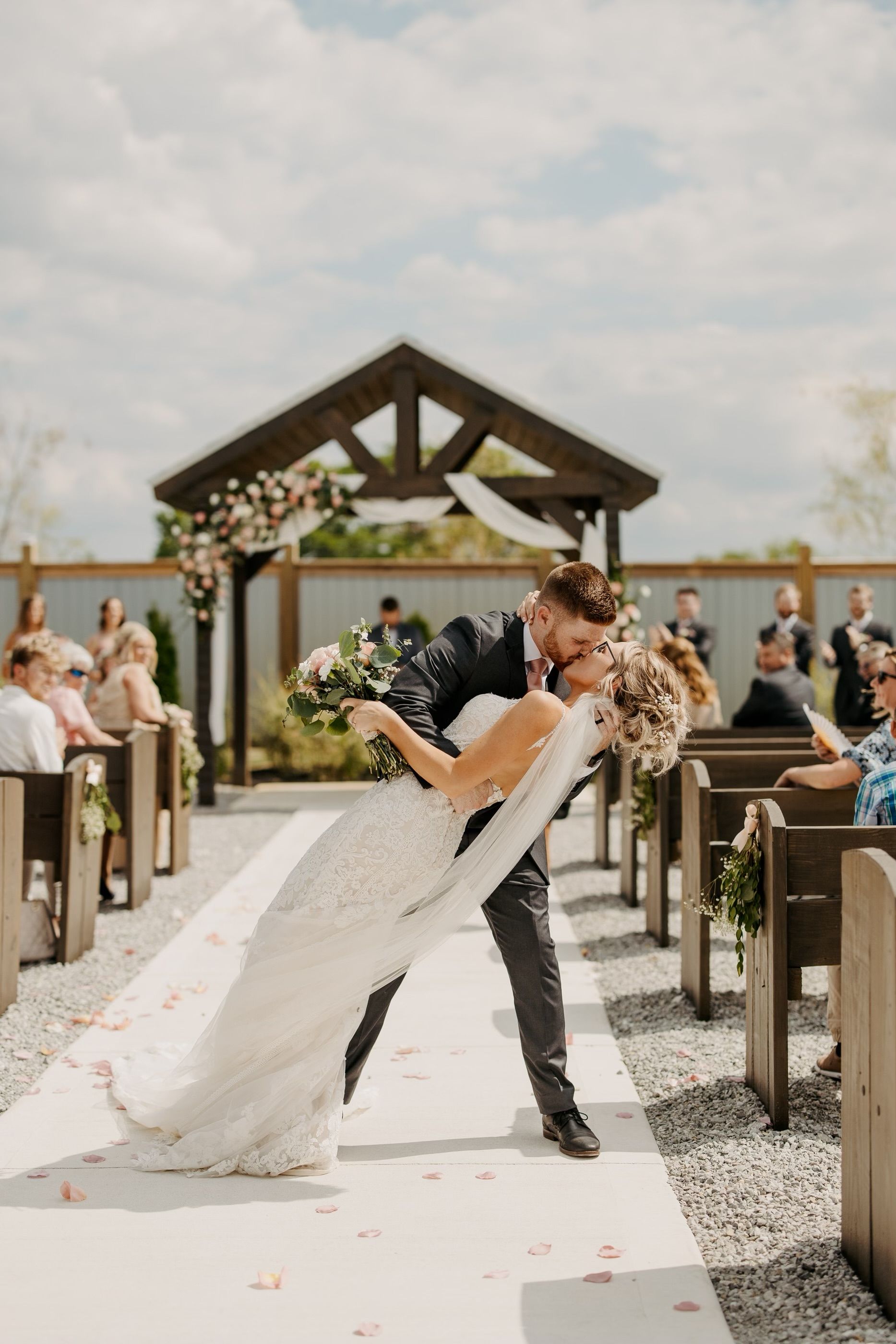 A bride and groom are kissing at their wedding ceremony in front of a church.
