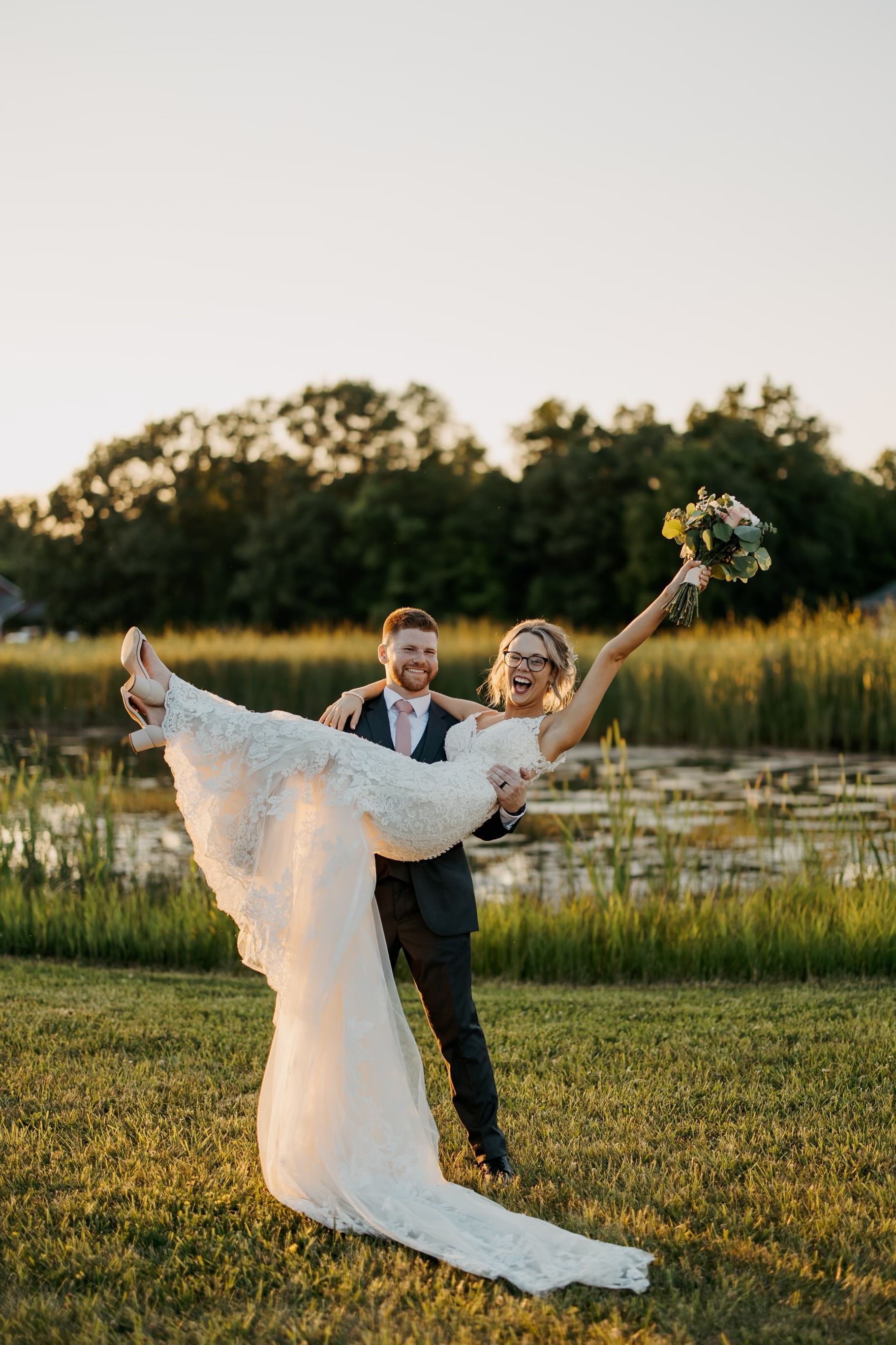 A man is holding a bride in his arms in a field.