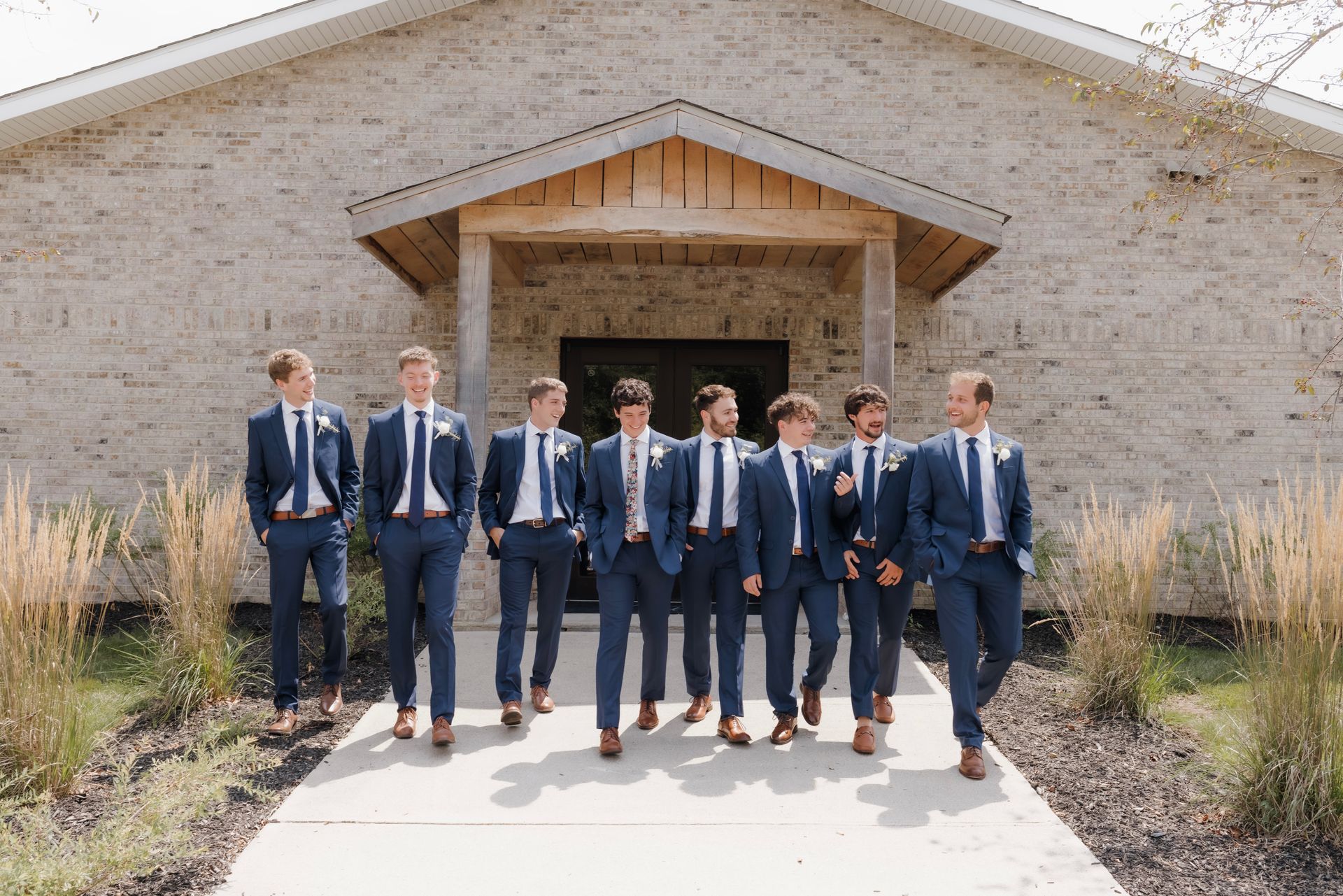A group of men in suits and ties are standing in front of a brick building.