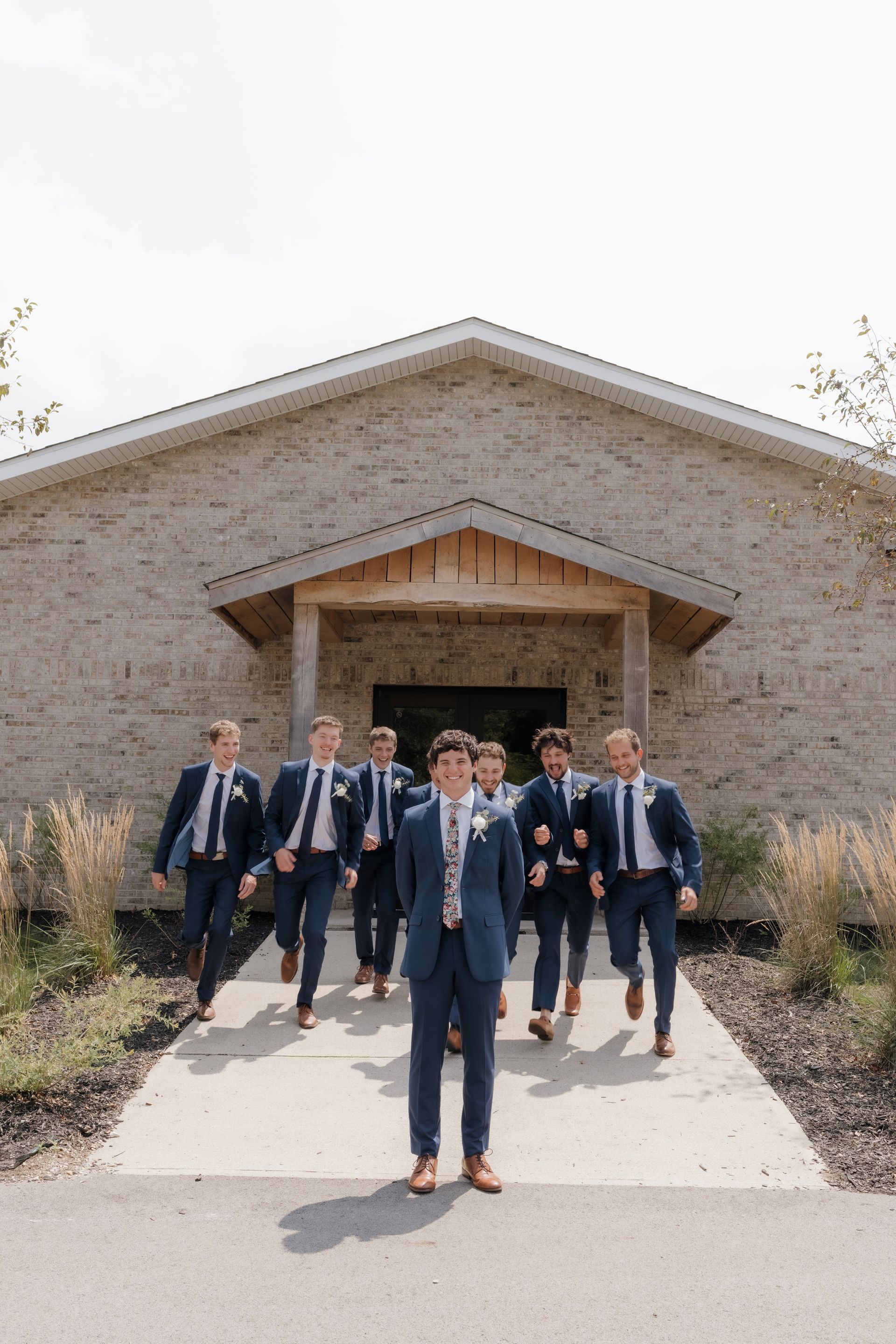 A groom and his groomsmen are walking down a sidewalk in front of a building.