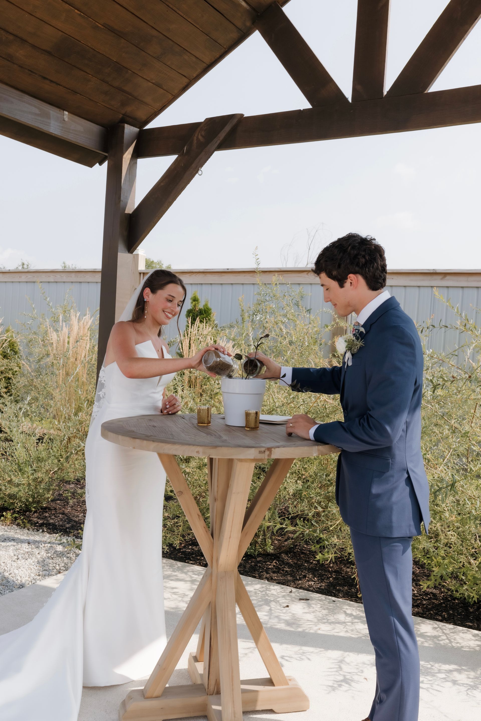 A bride and groom are standing at a table under a canopy.