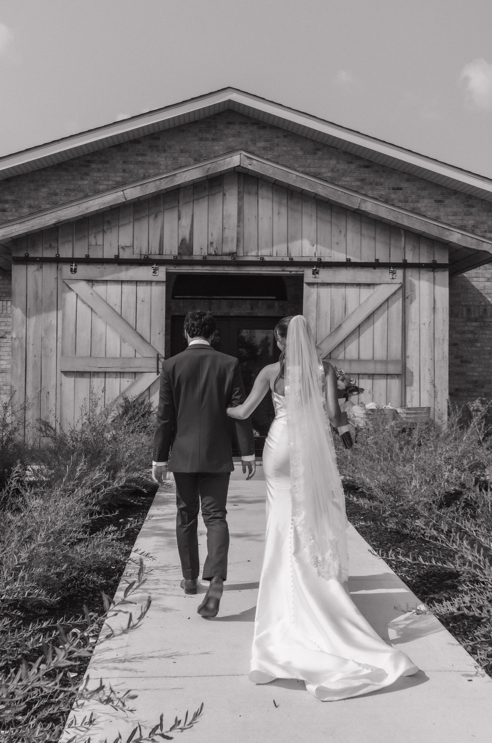 A black and white photo of a bride and groom walking down a path.