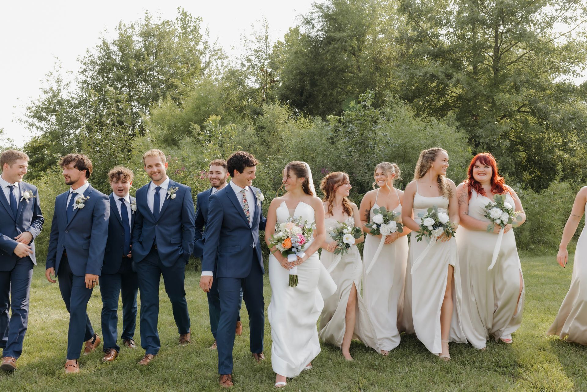 A bride and groom are walking with their wedding party in a field.