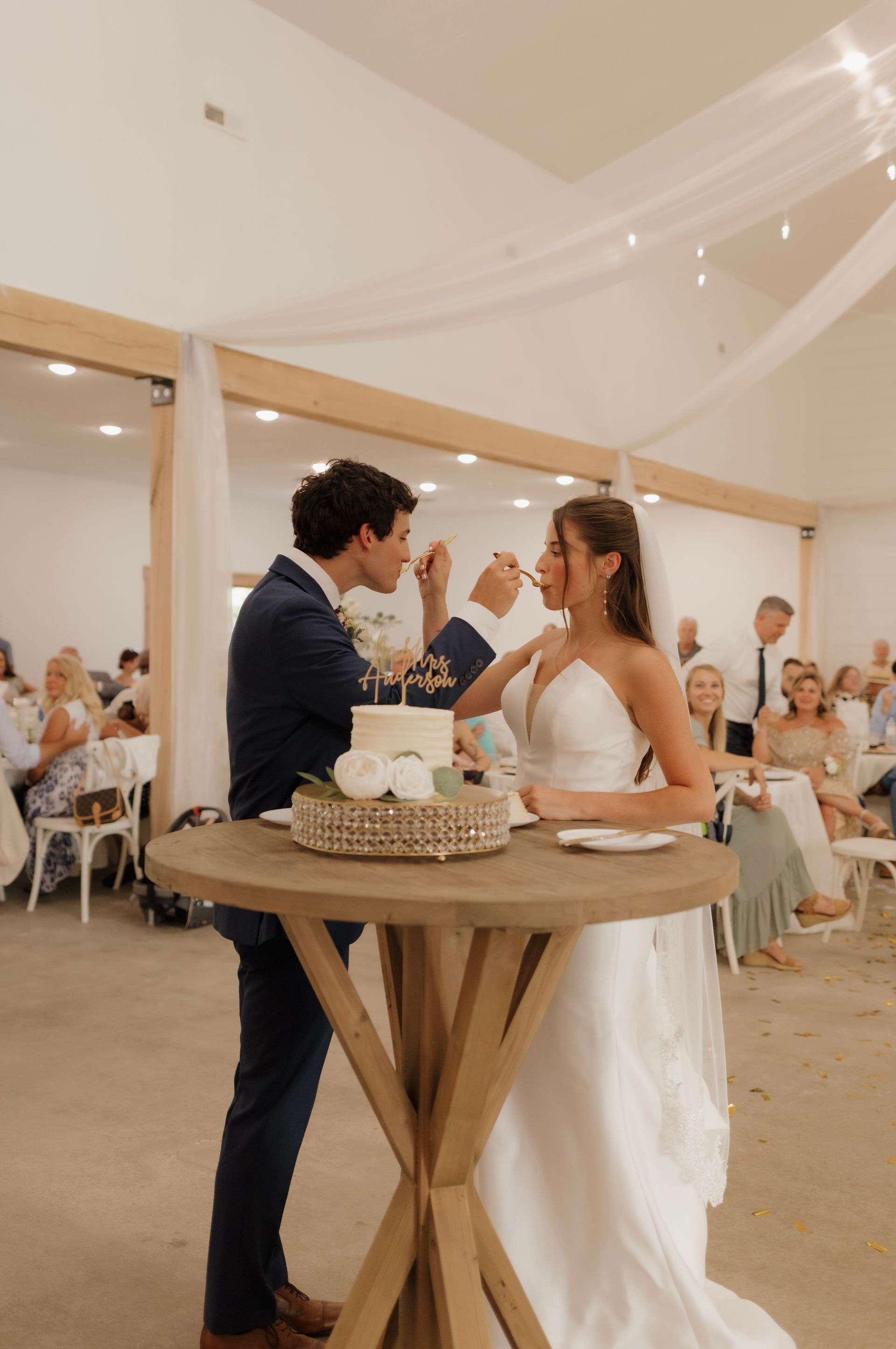 A bride and groom are cutting their wedding cake at a table.
