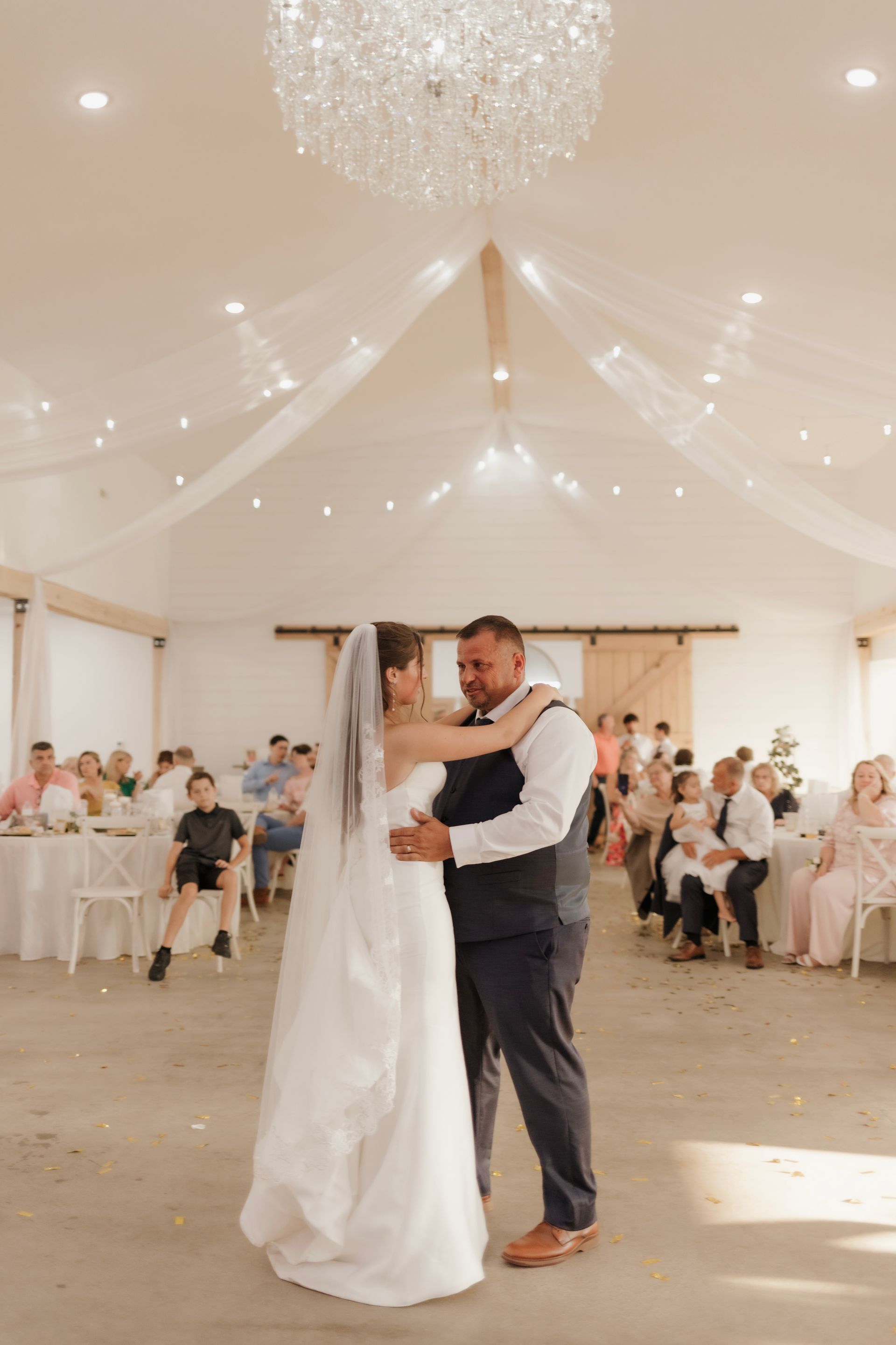 A bride and groom are dancing in a large room at their wedding reception.