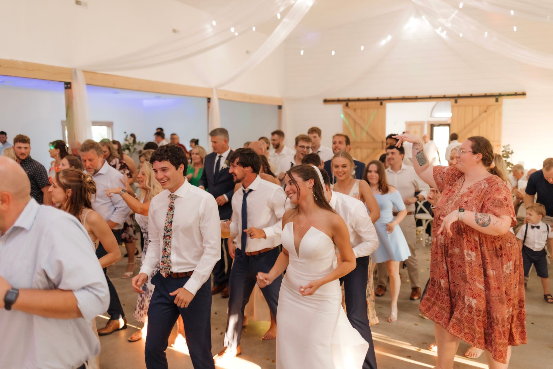 A large group of people are dancing at a wedding reception.