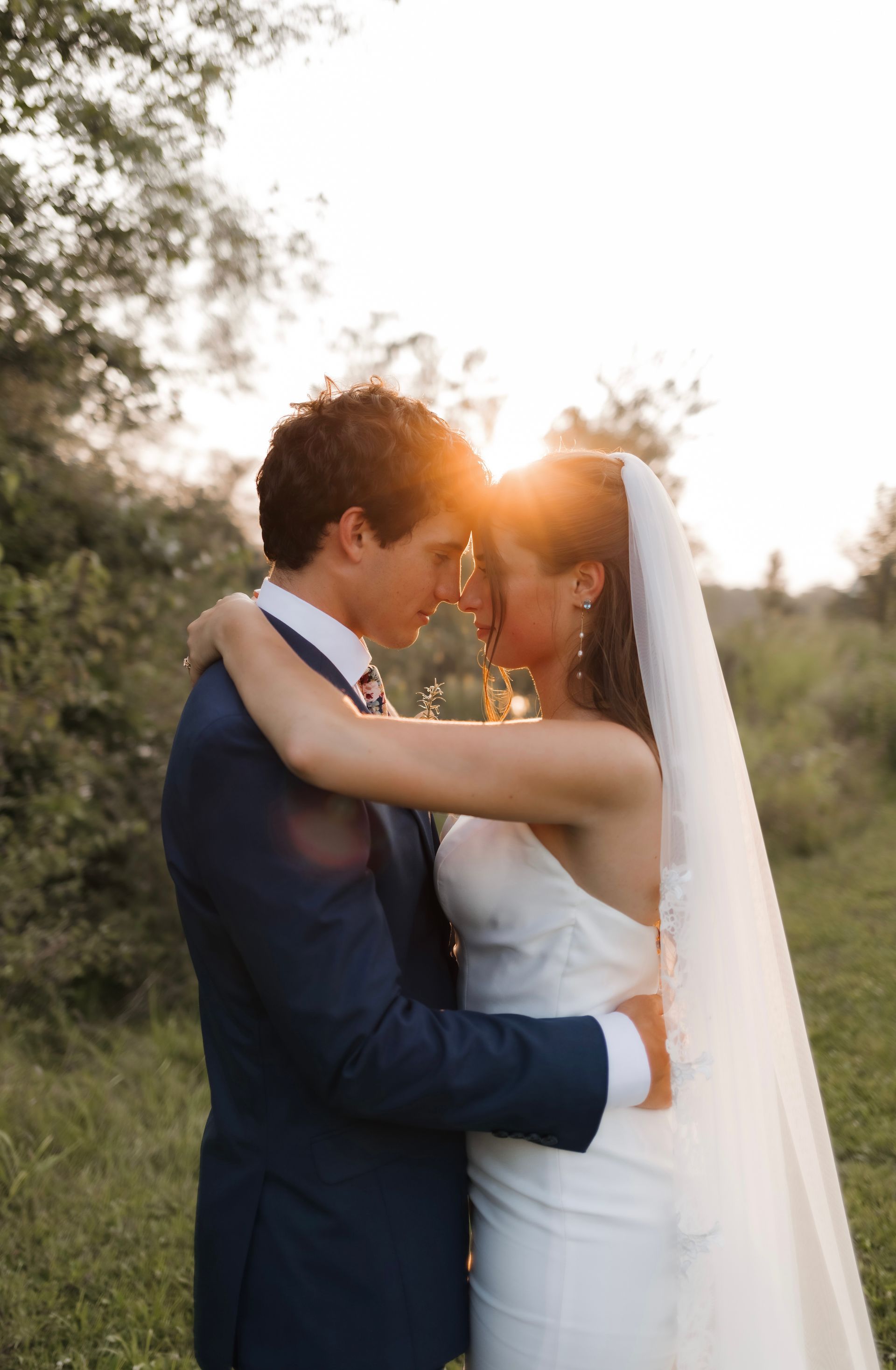 A bride and groom are hugging and looking at each other in a field.