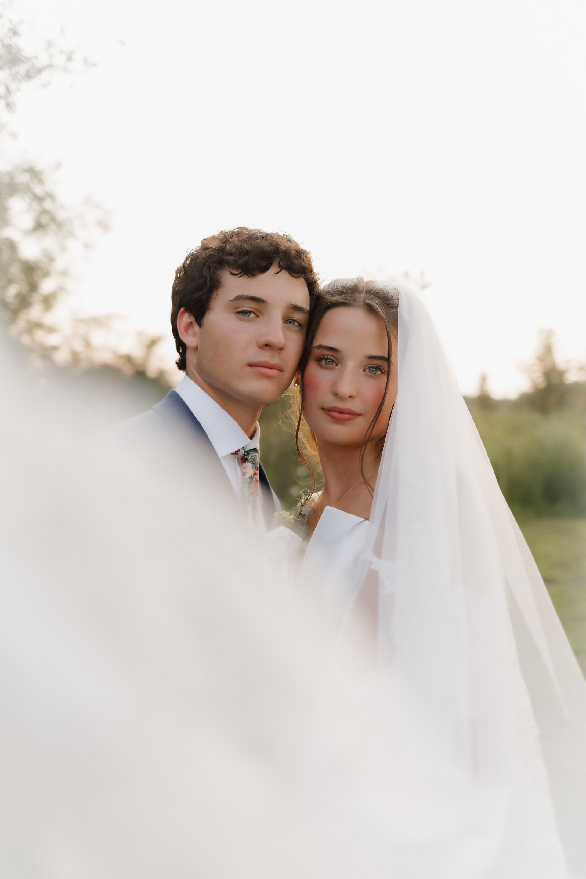 A bride and groom are posing for a picture under a veil.
