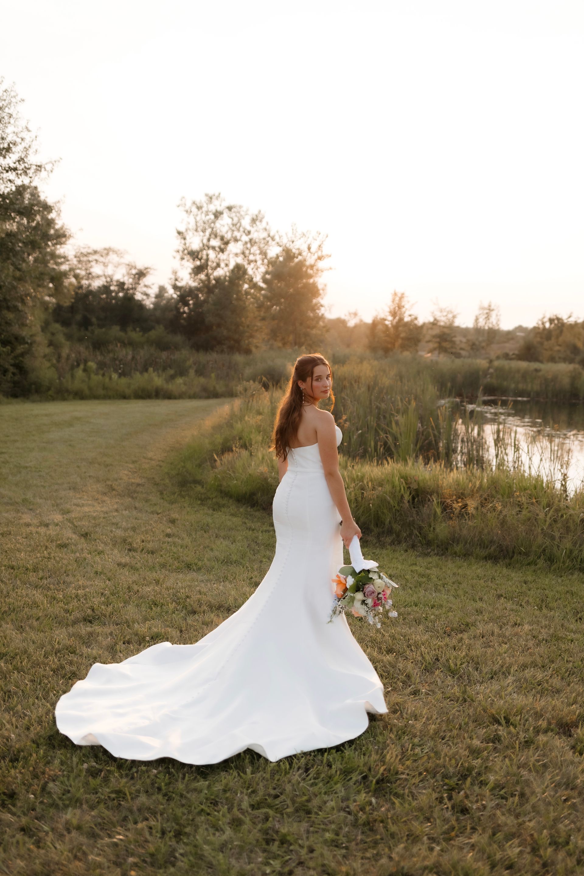 A bride in a white wedding dress is standing in a field holding a bouquet of flowers.