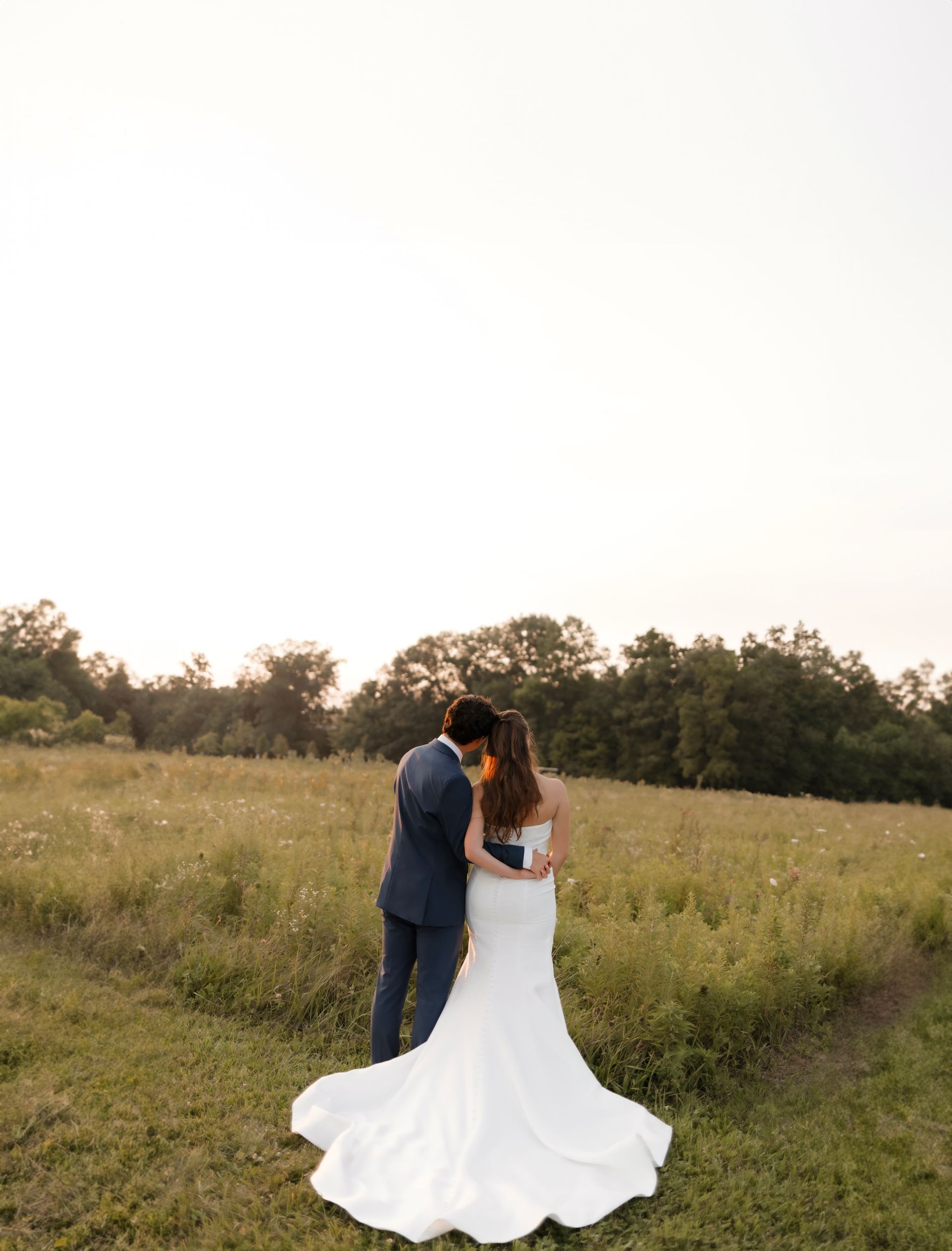 A bride and groom are standing in a field.