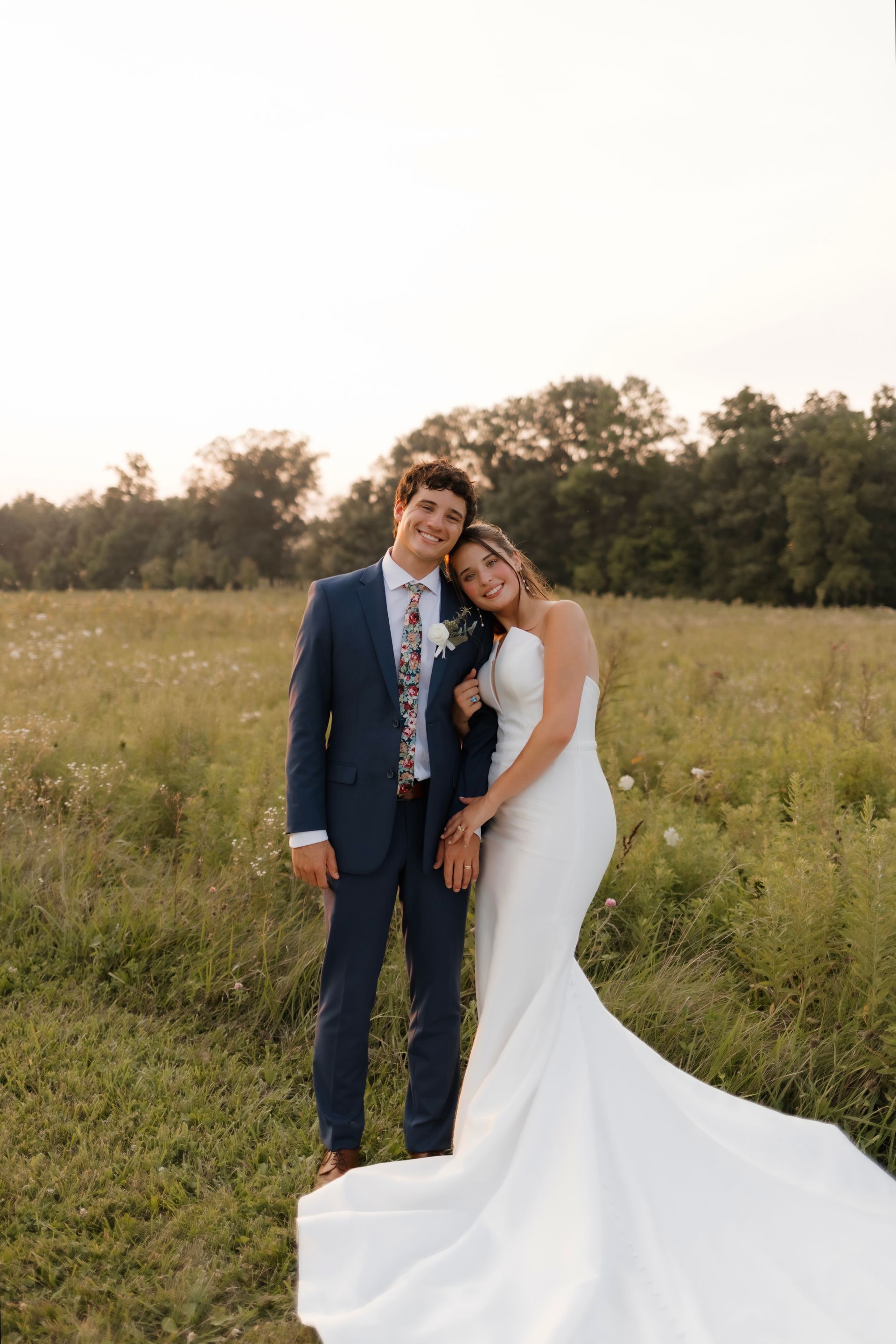 A bride and groom are posing for a picture in a field.
