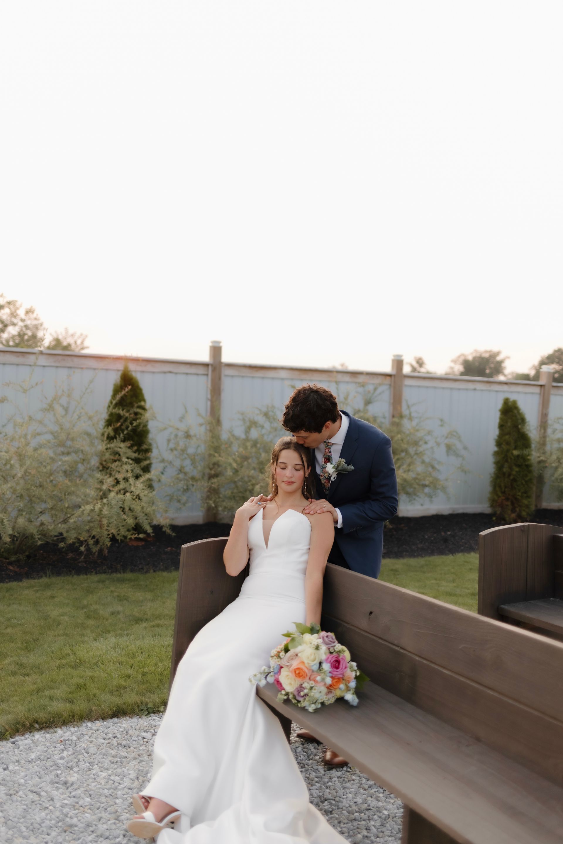 A bride and groom are posing for a picture while sitting on a bench.