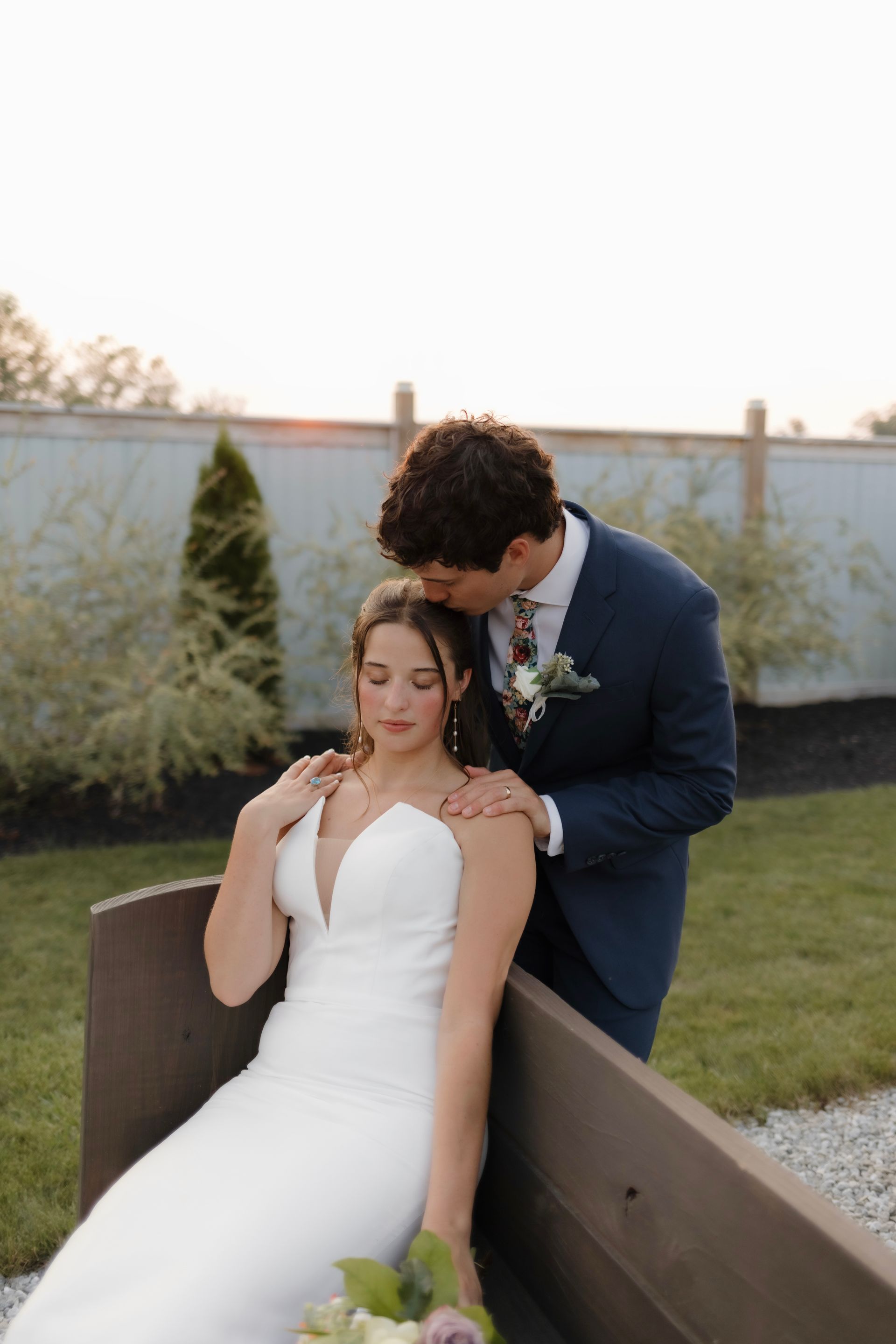A bride and groom are posing for a picture on a bench.