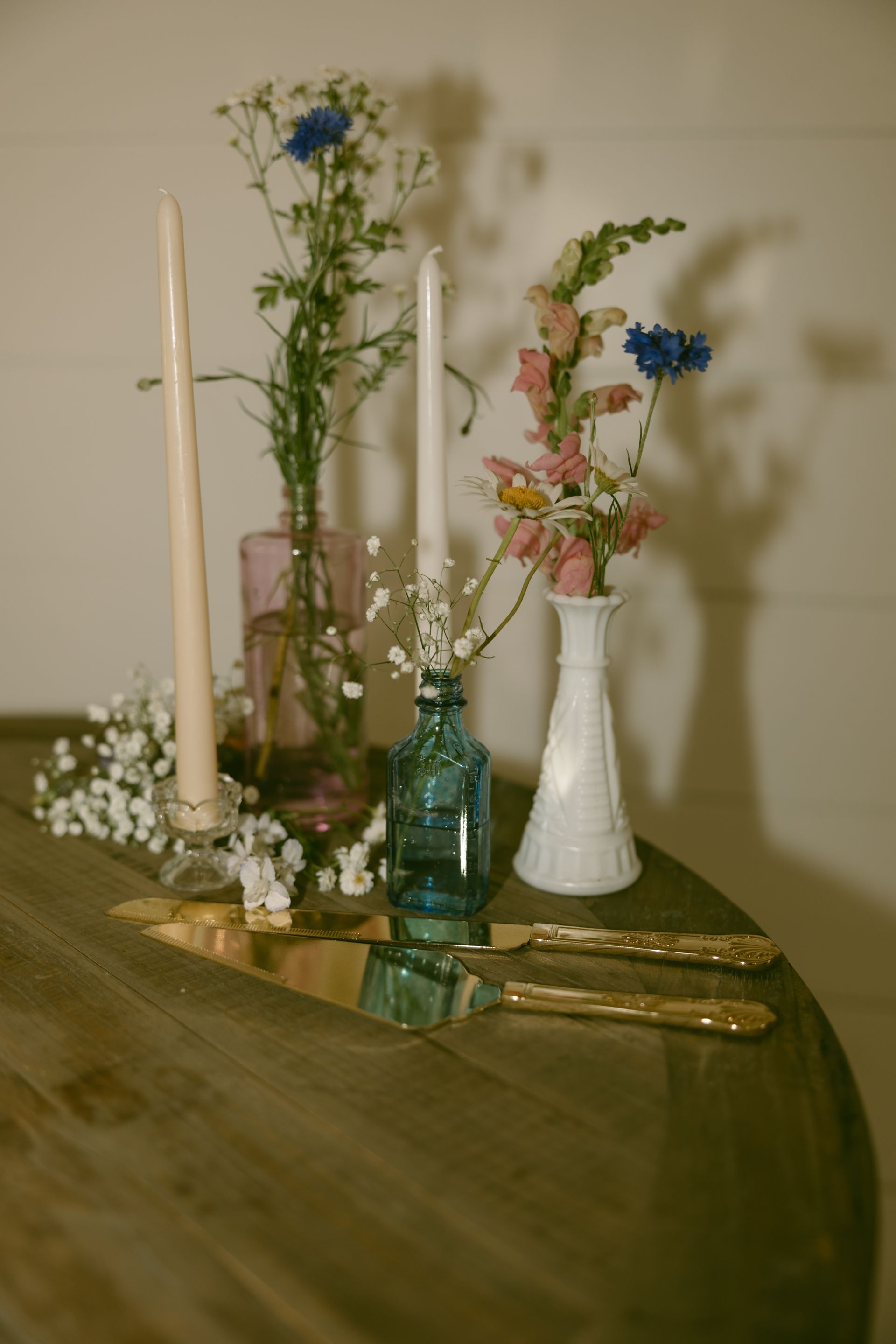 A table with a vase of flowers , candles , and silverware on it.