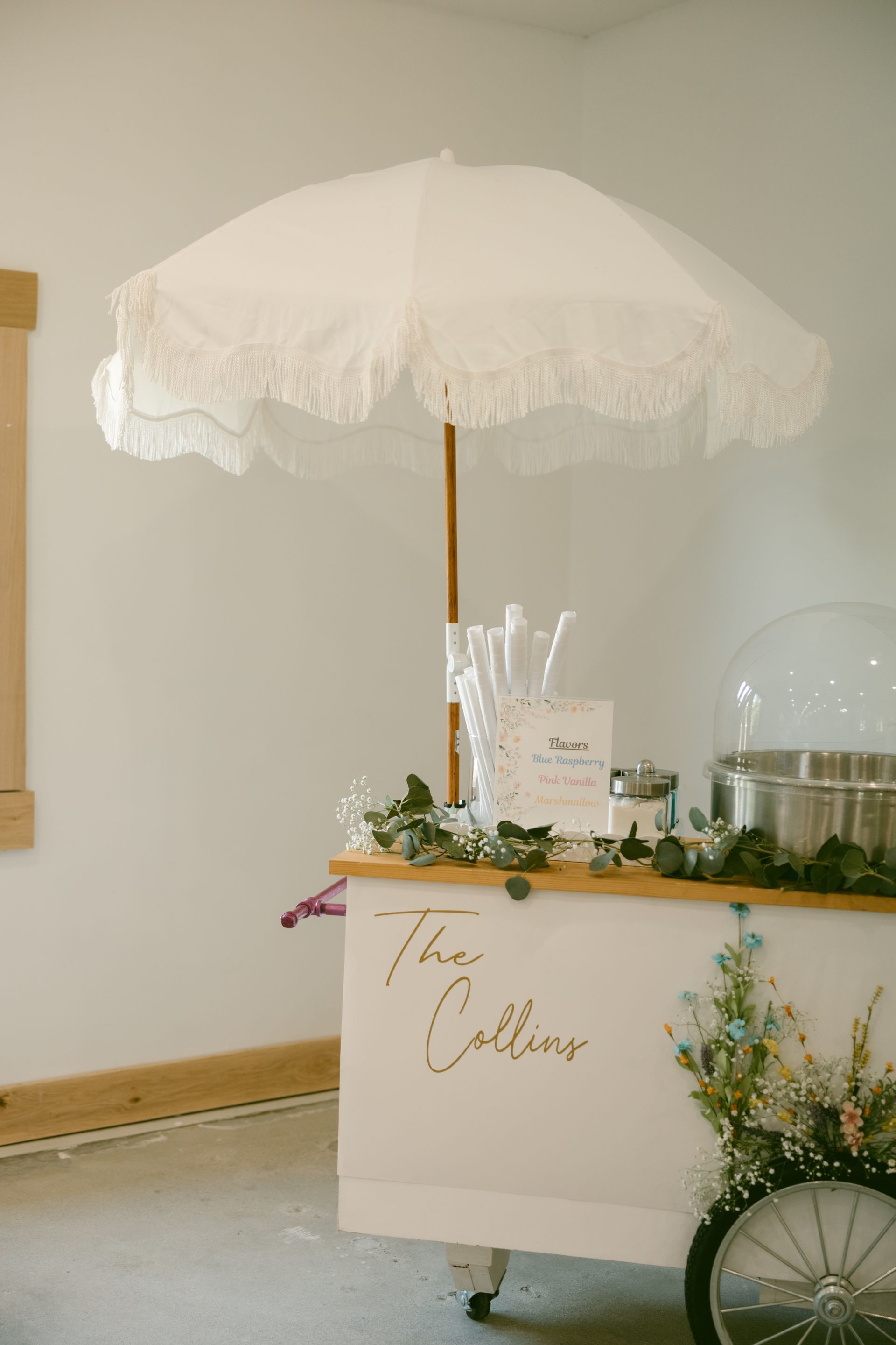 A white cart with a white umbrella and cotton candy on it.