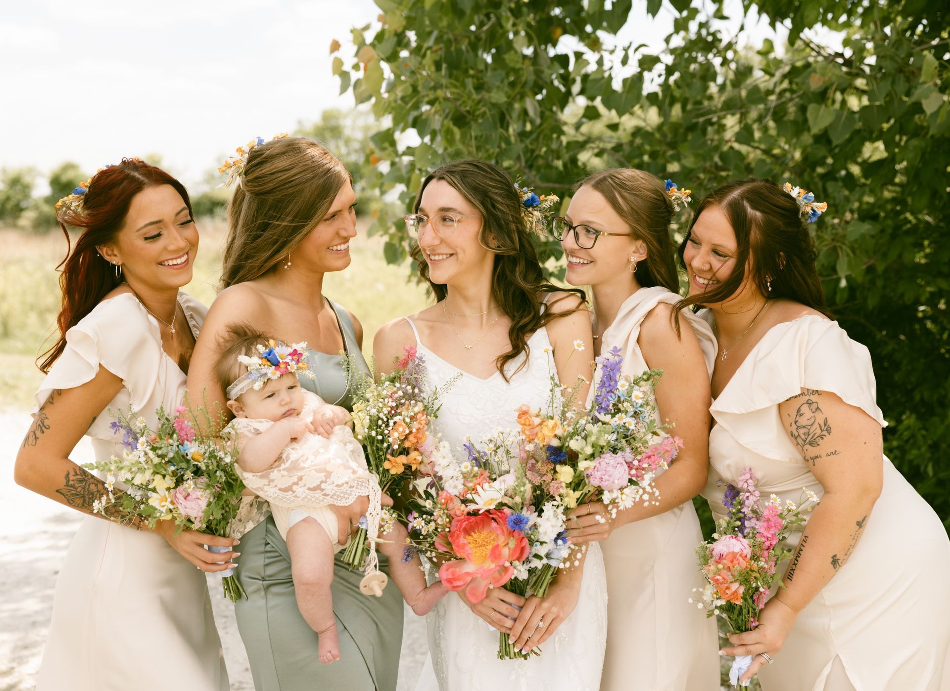 A bride and her bridesmaids are posing for a picture with a baby.
