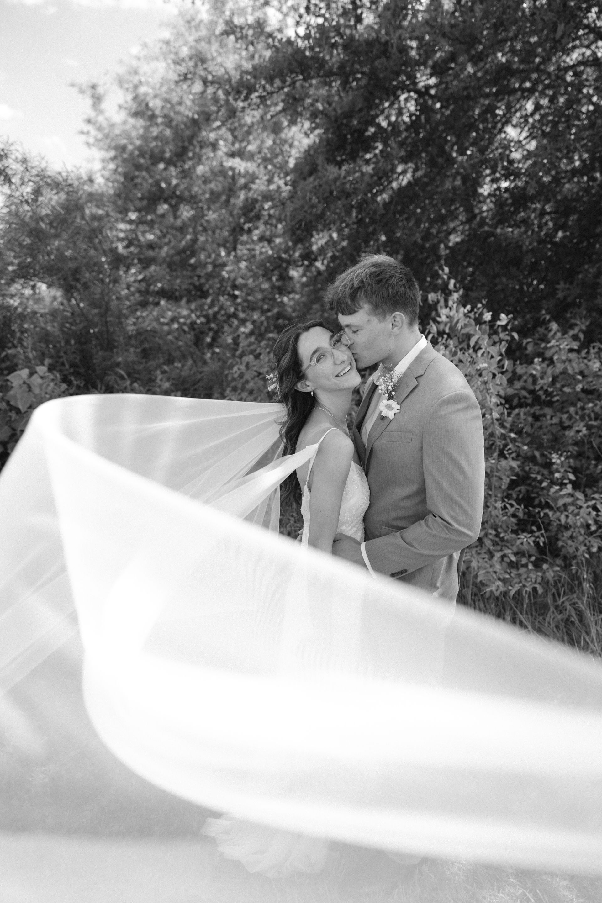 A black and white photo of a bride and groom with a veil blowing in the wind.