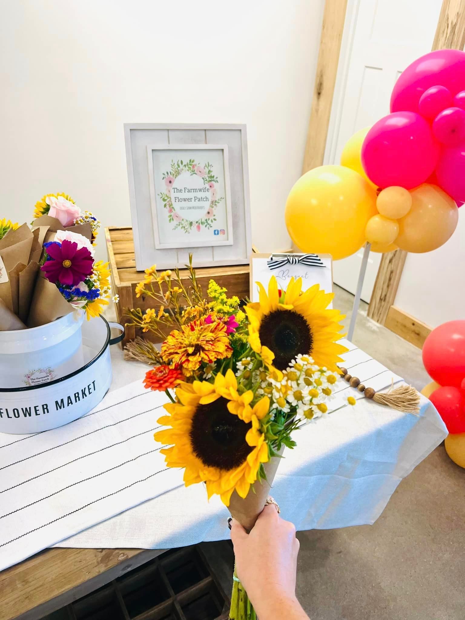 A person is holding a bouquet of sunflowers on a table with balloons.