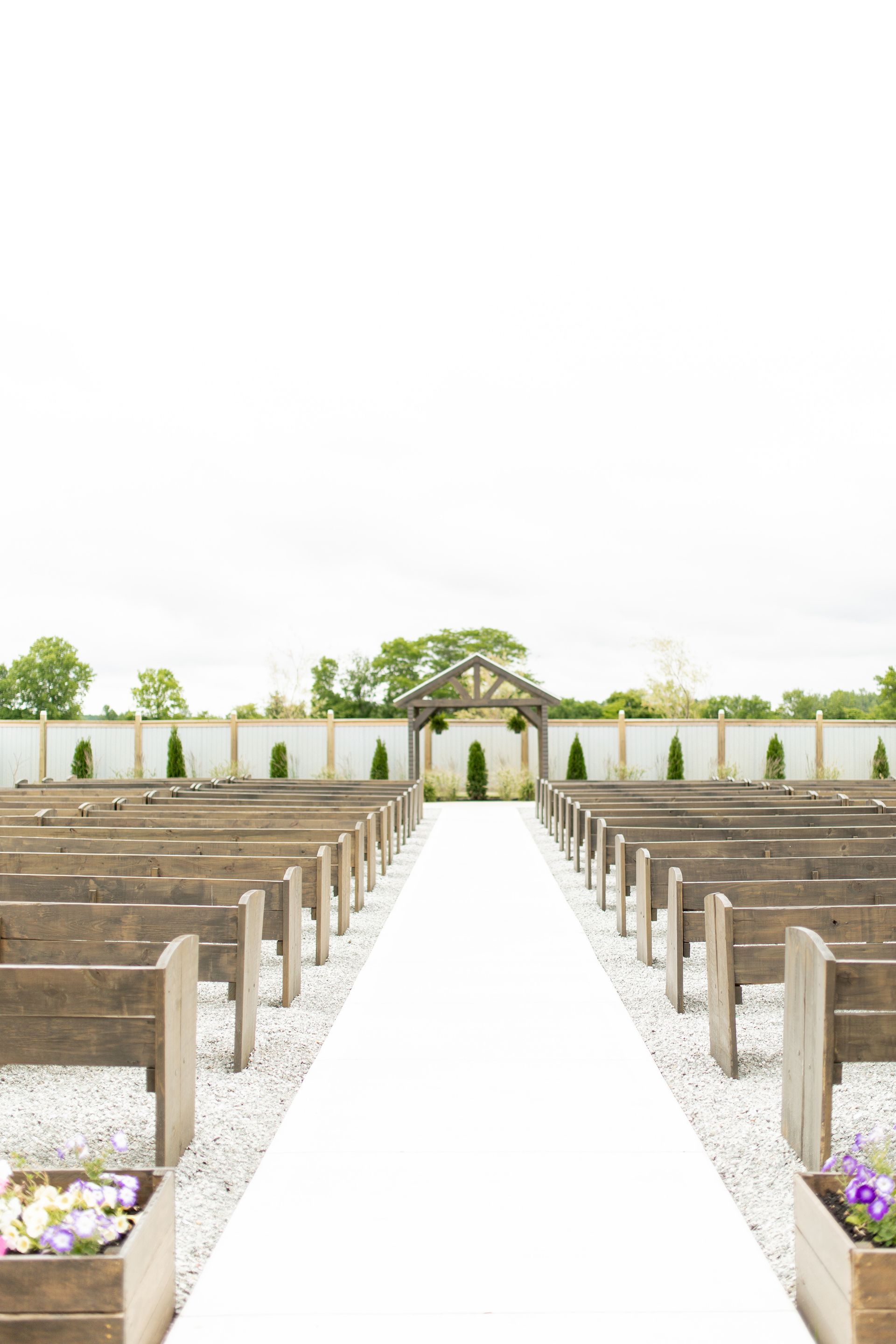 A white aisle leading to a wedding ceremony with wooden benches.