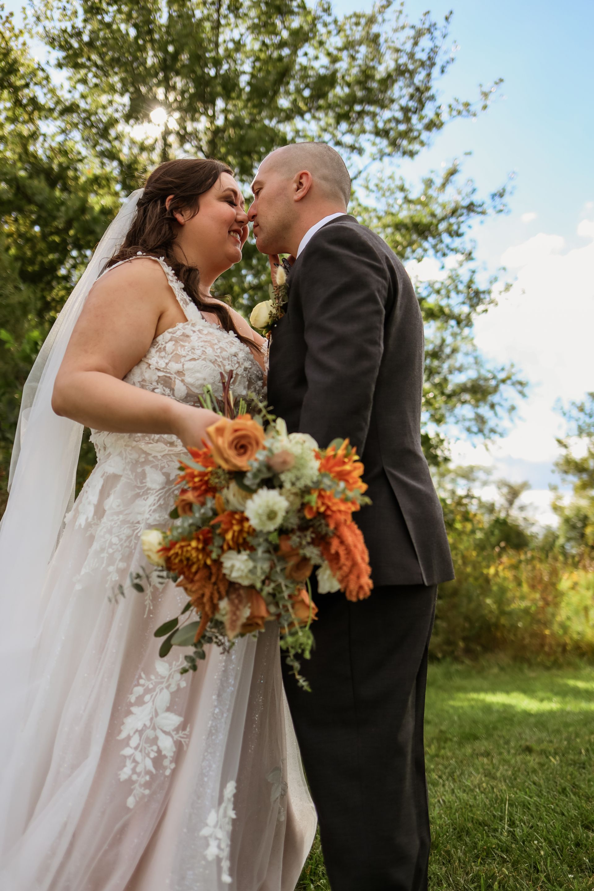 A bride and groom are kissing in a field while holding a bouquet of flowers.