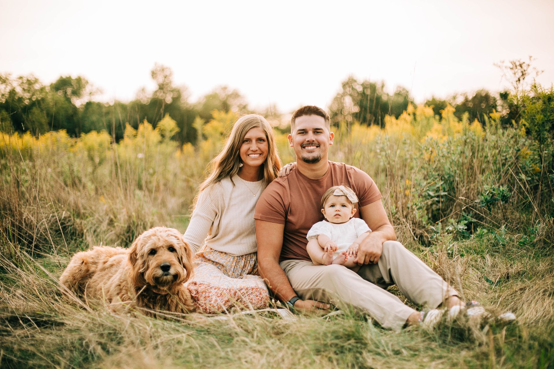 A family is sitting in a field with a dog and a baby.