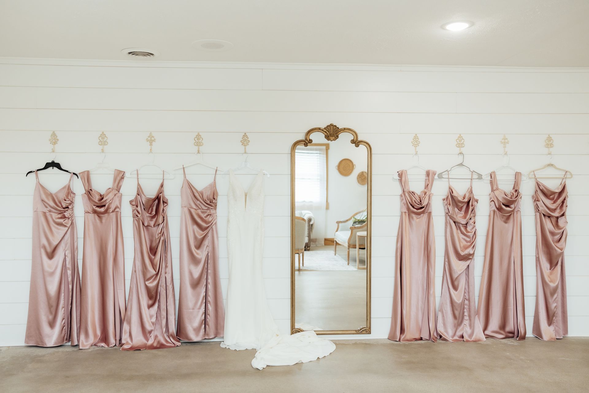 A row of pink bridesmaid dresses hanging on a wall next to a mirror.