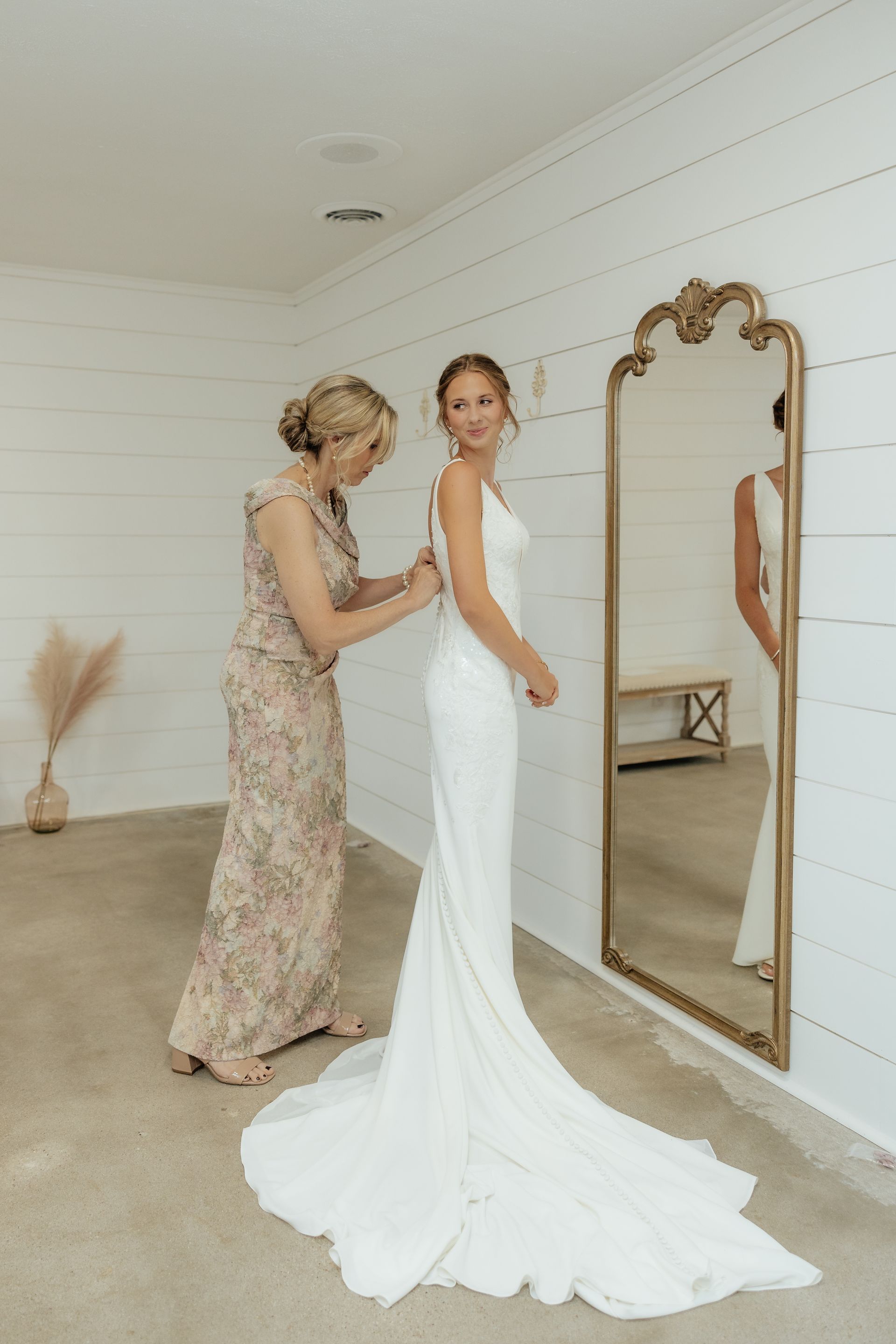A woman is helping a bride get ready for her wedding in front of a mirror.