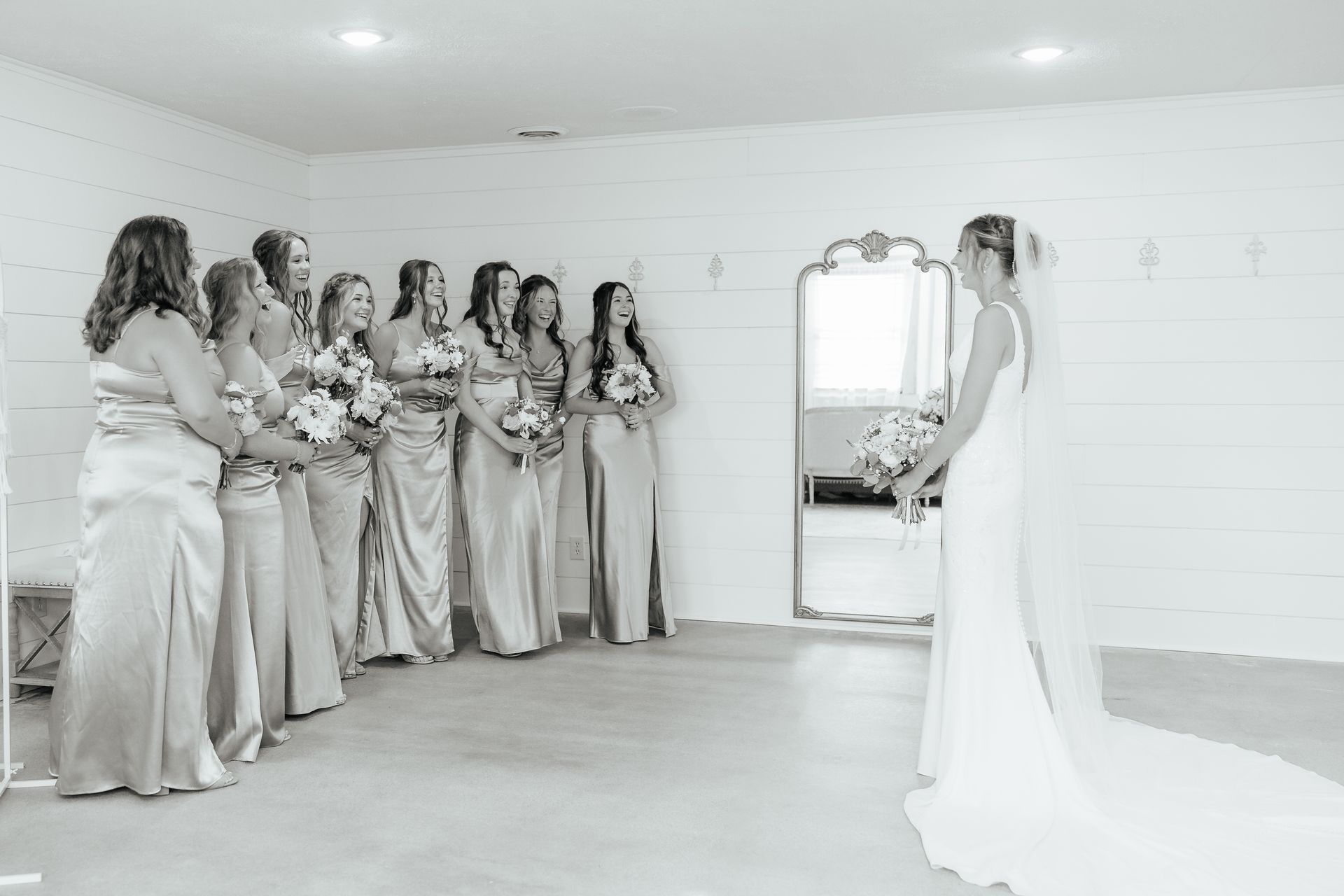 A bride and her bridesmaids are standing in front of a mirror in a room.