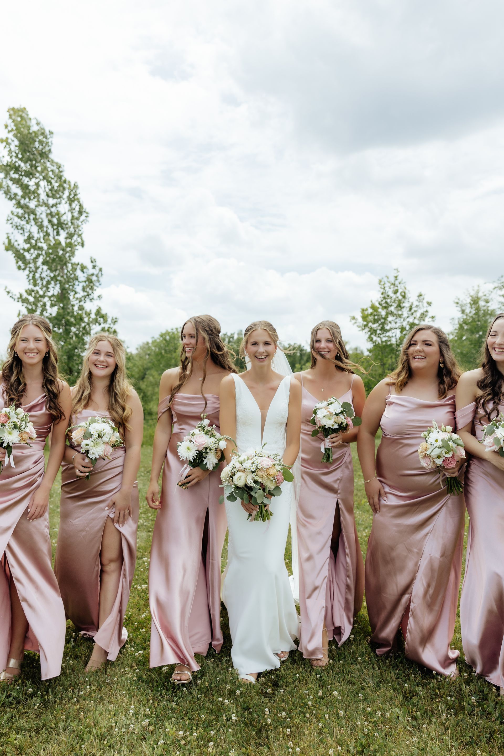 A bride and her bridesmaids are posing for a picture in a field.