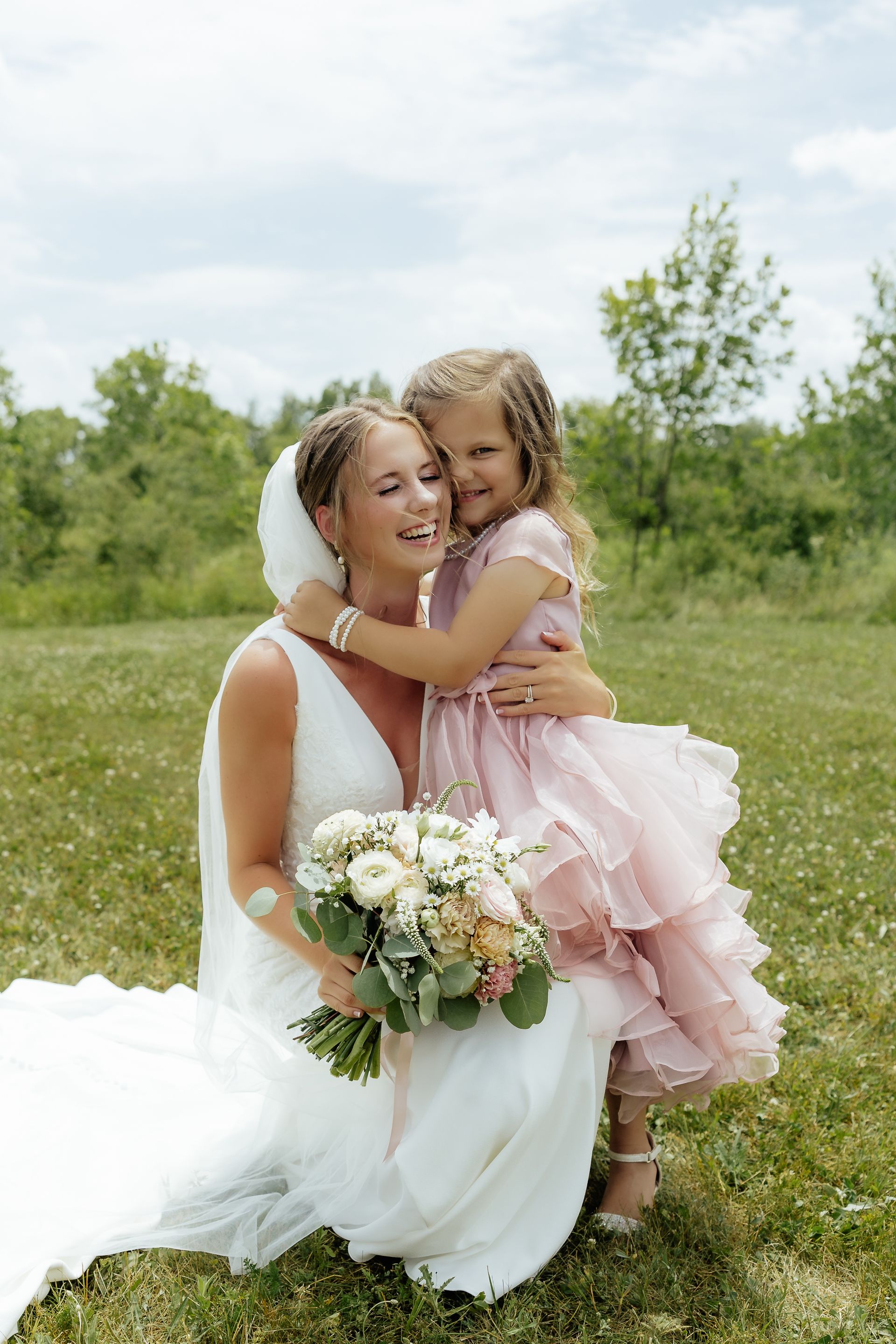 A bride and her flower girl are posing for a picture in a field.