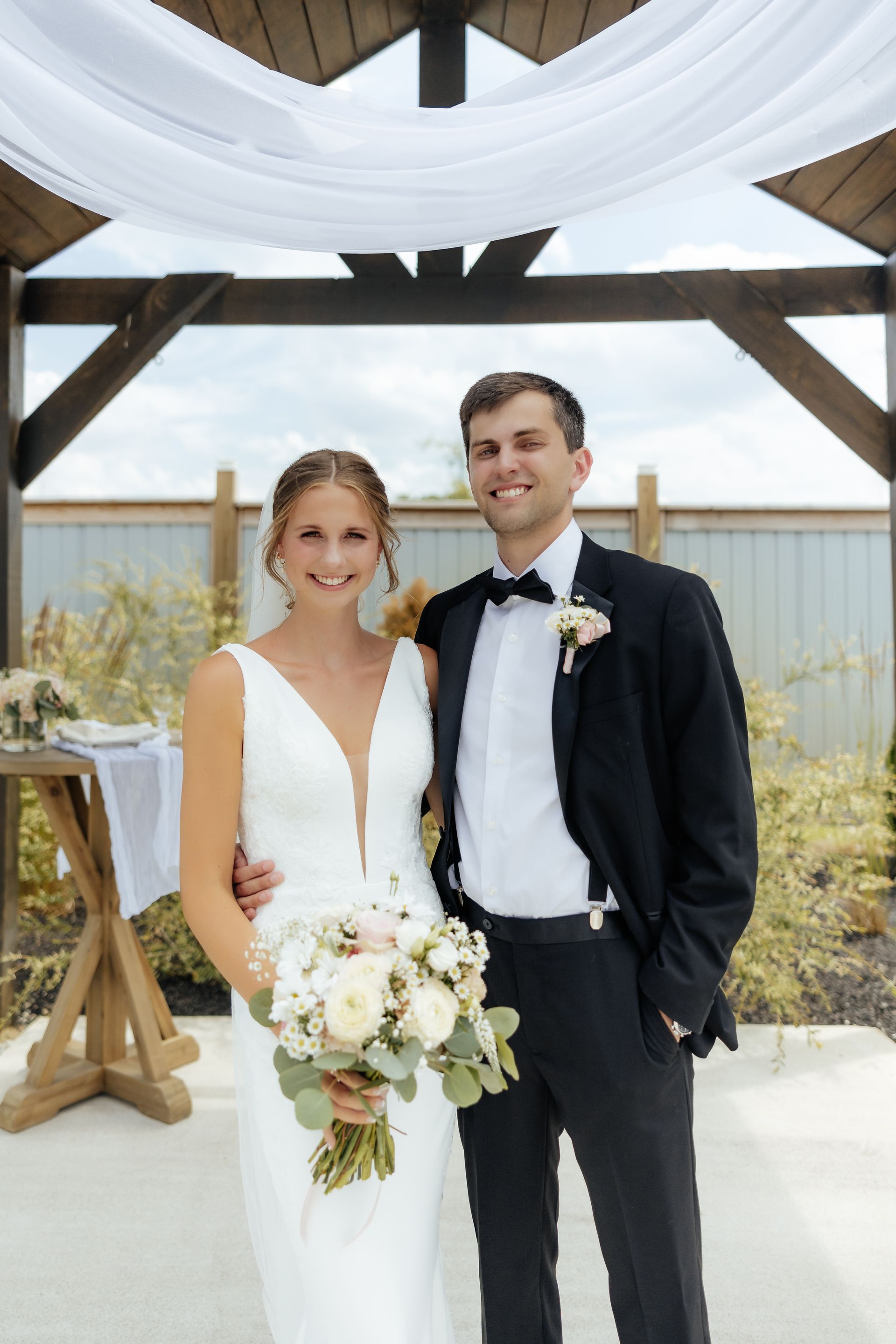 A bride and groom are posing for a picture under a gazebo.
