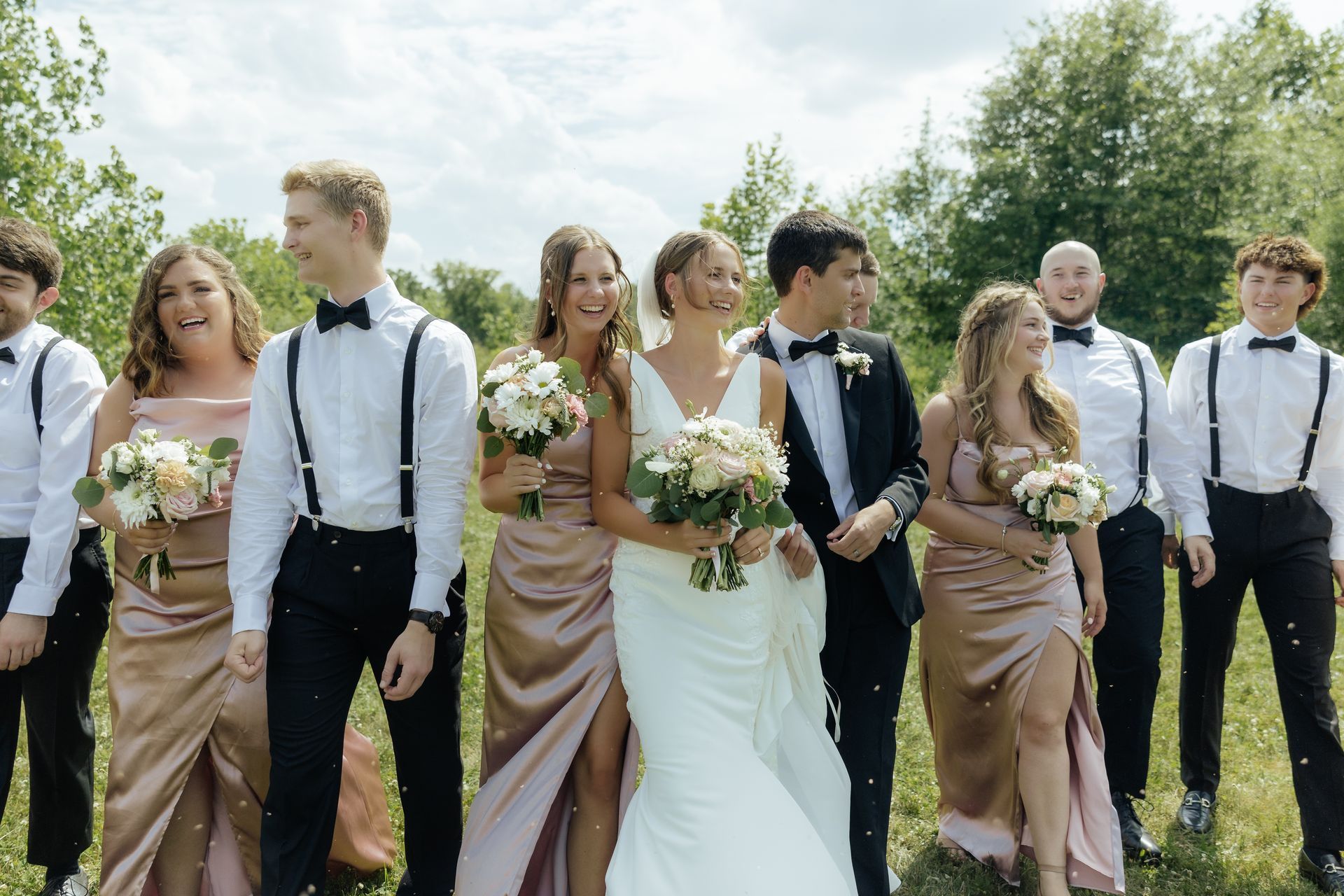 A bride and groom are walking with their wedding party in a field.