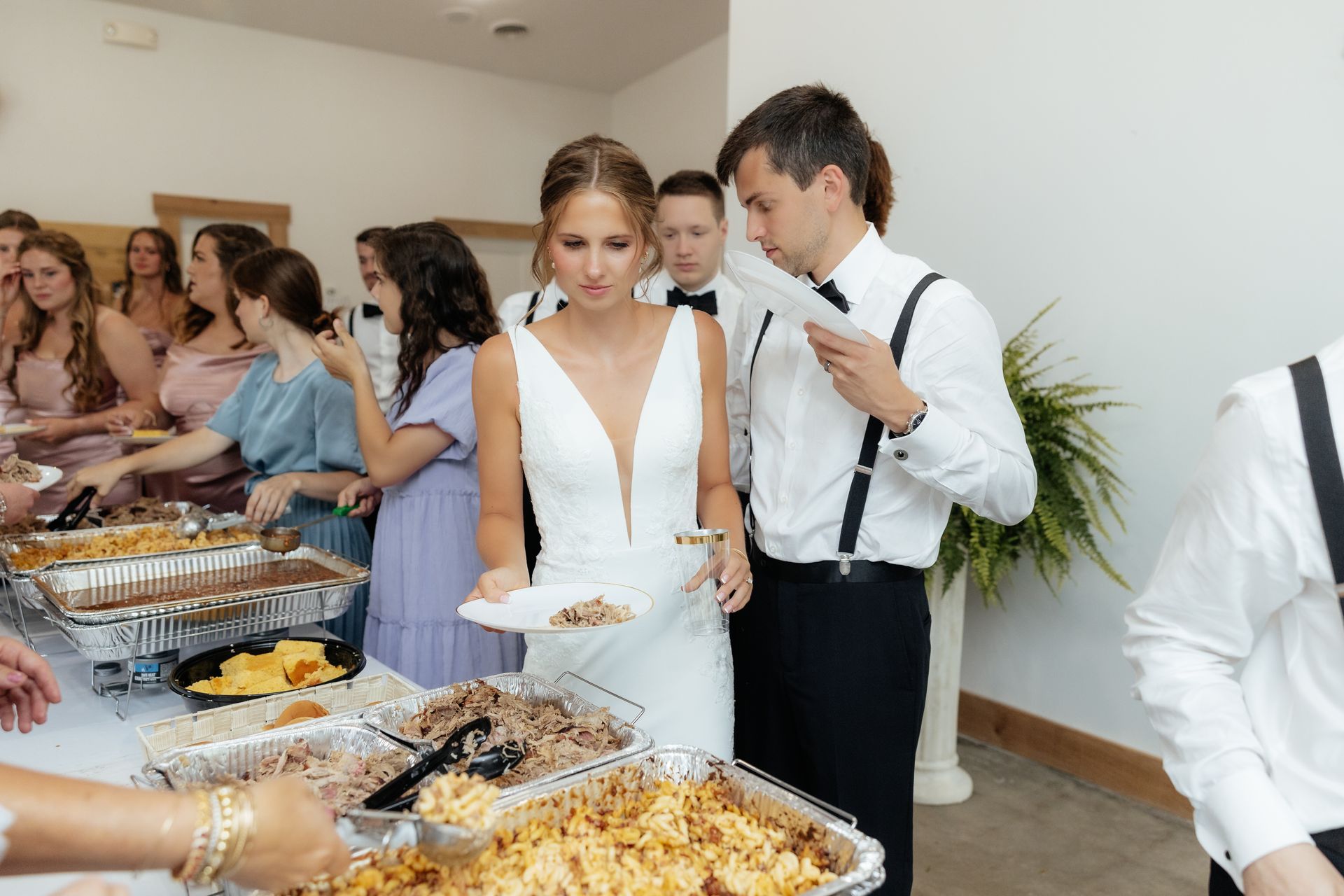 A bride and groom are standing in front of a buffet line at a wedding reception.