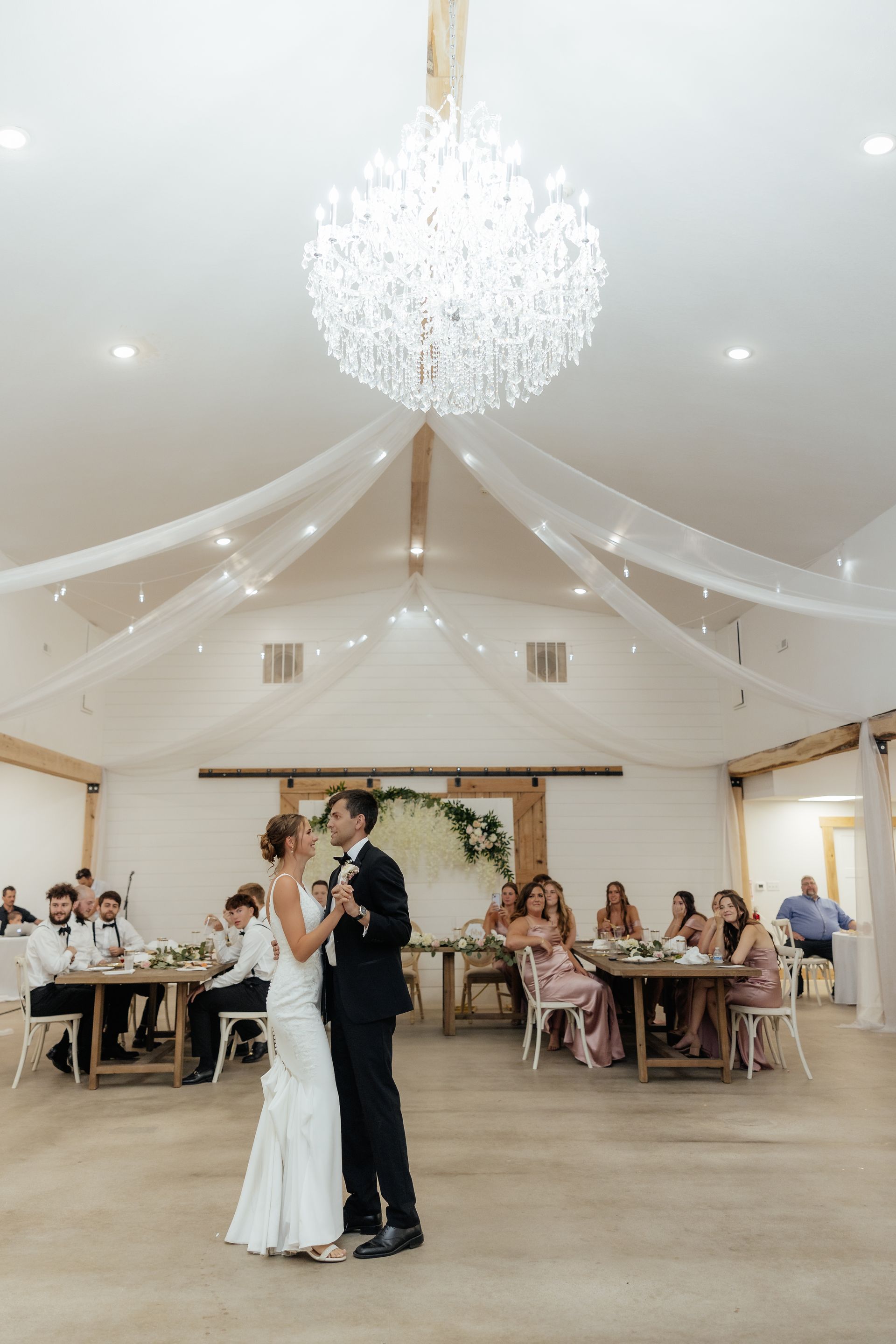 A bride and groom are dancing in a large room at their wedding reception.
