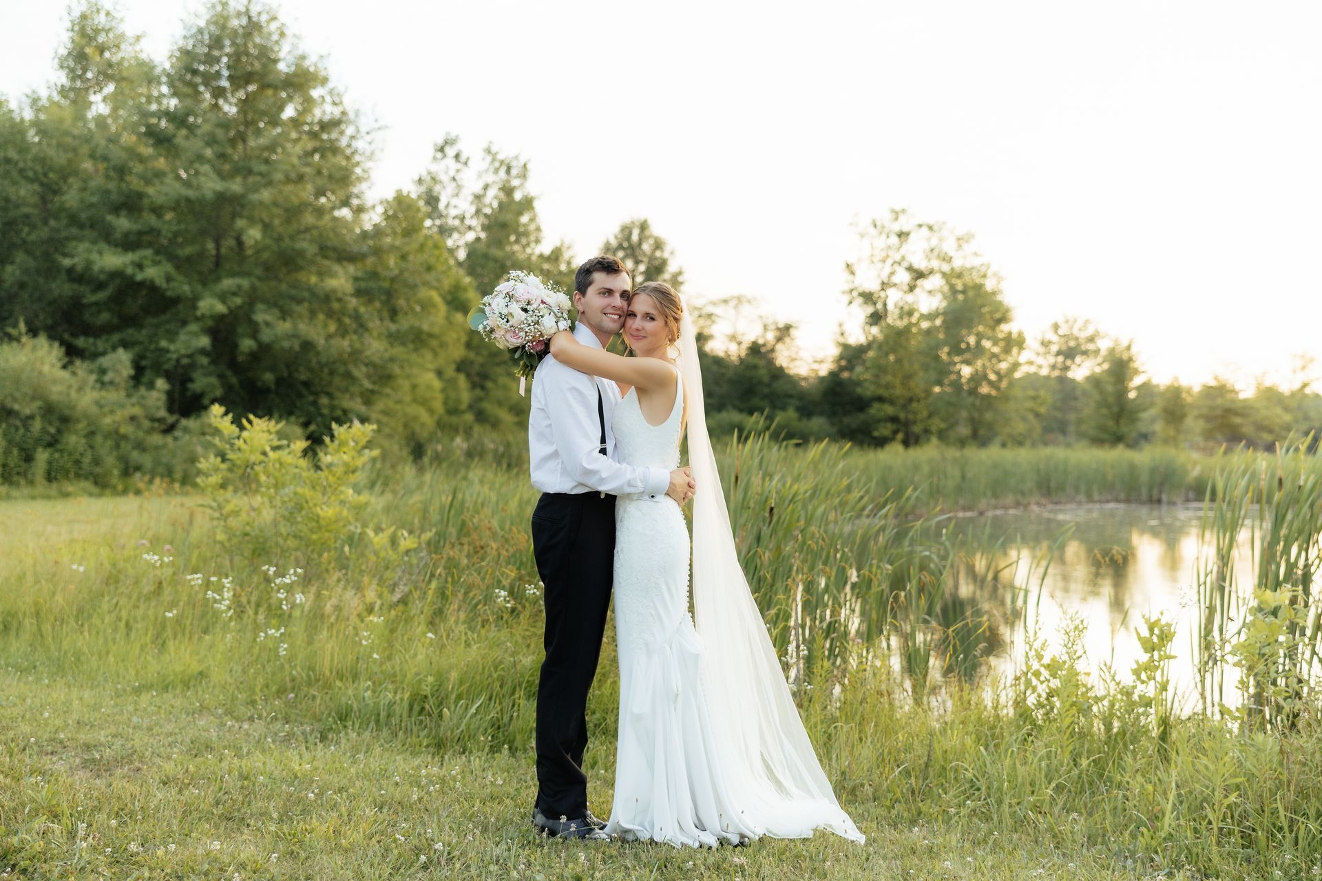 A bride and groom are posing for a picture in front of a lake.