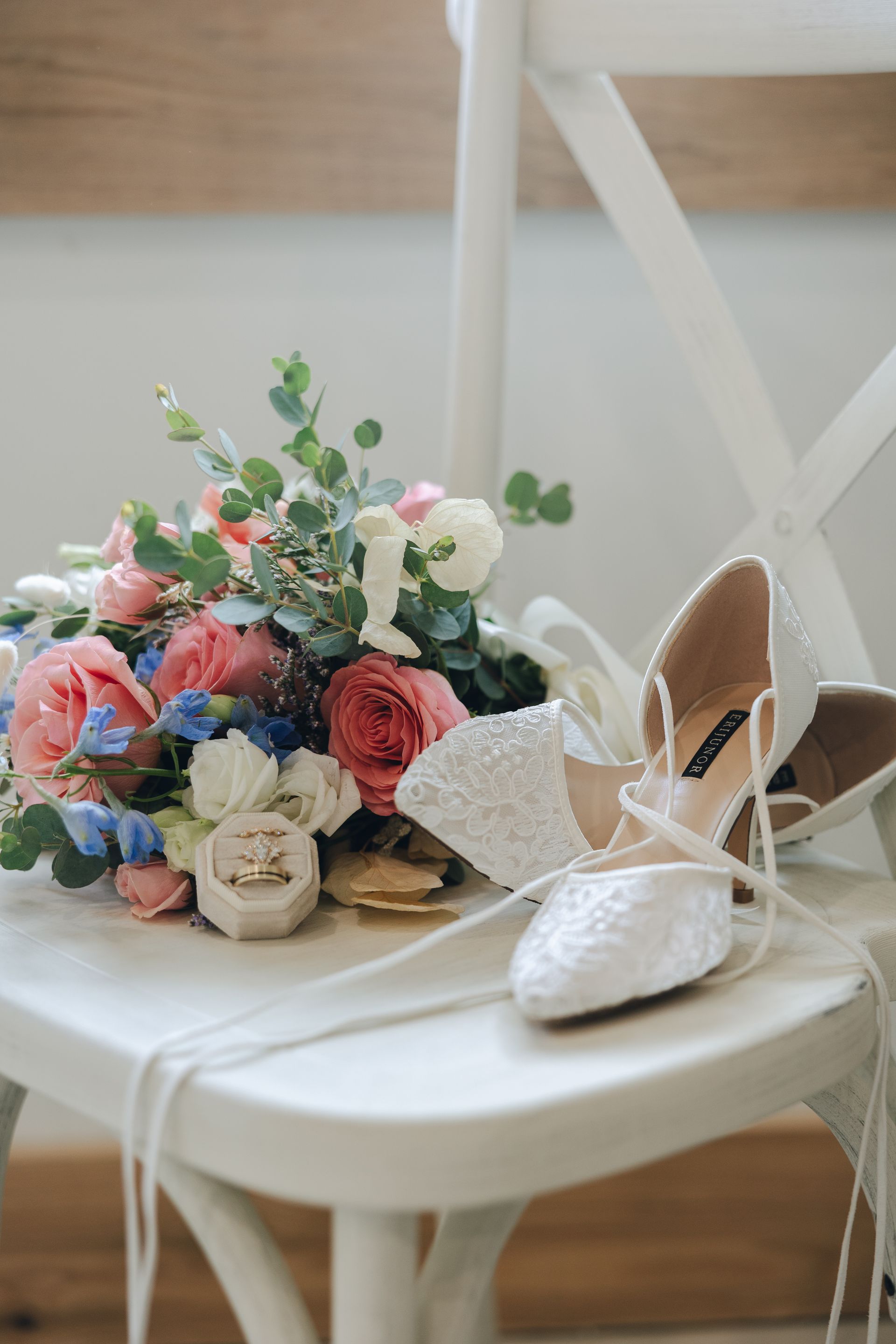 A bouquet of flowers and wedding shoes are sitting on a white chair.